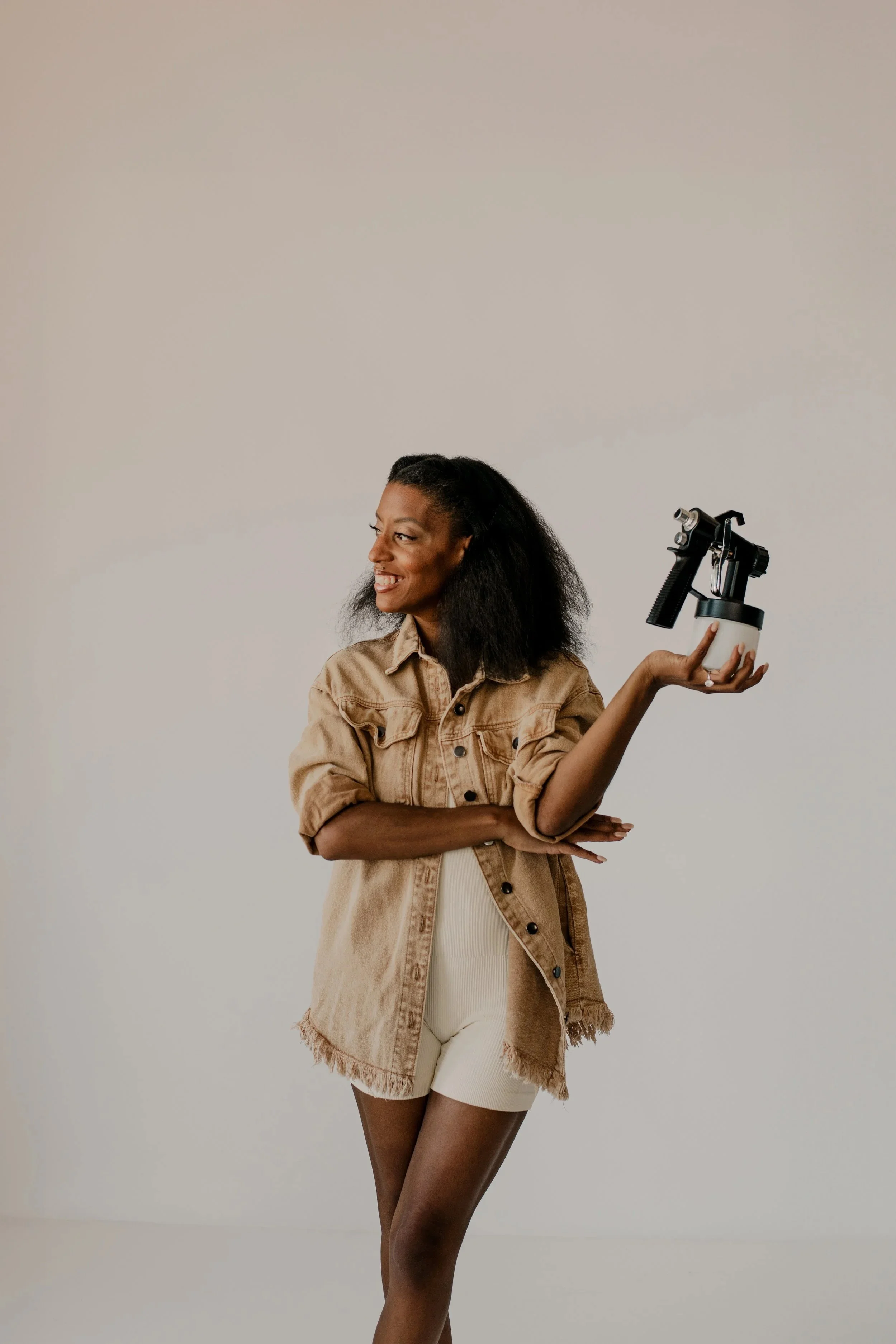 A woman standing in front of a white backdrop looking off to the side while she is holding a tanning bottle in BrushCo Studio in Kansas City, Missouri