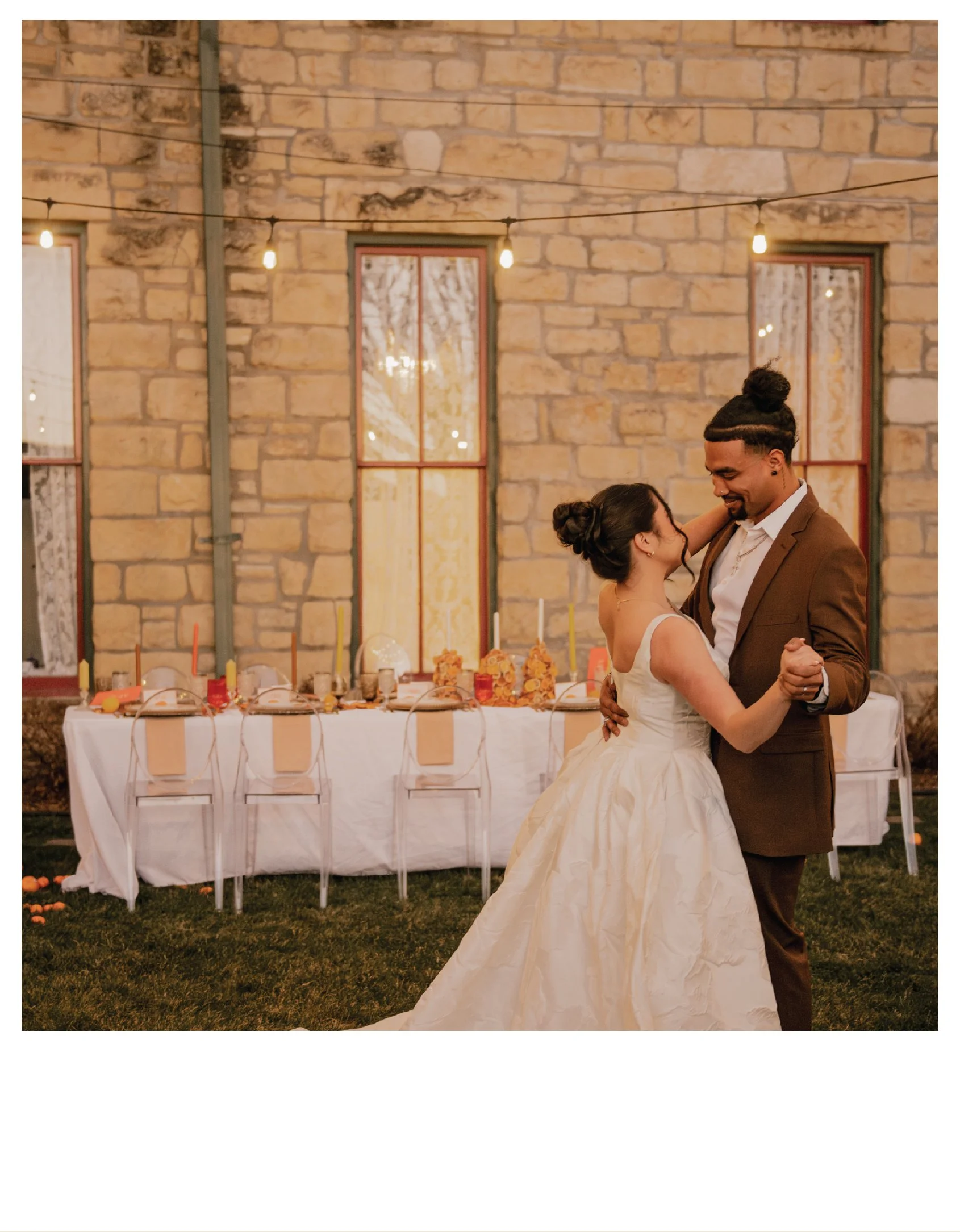 A bride and groom dancing outside at sunset, with a decorated table and string lights in the background at the Historic Elgin Hotel in Kansas City, Missouri