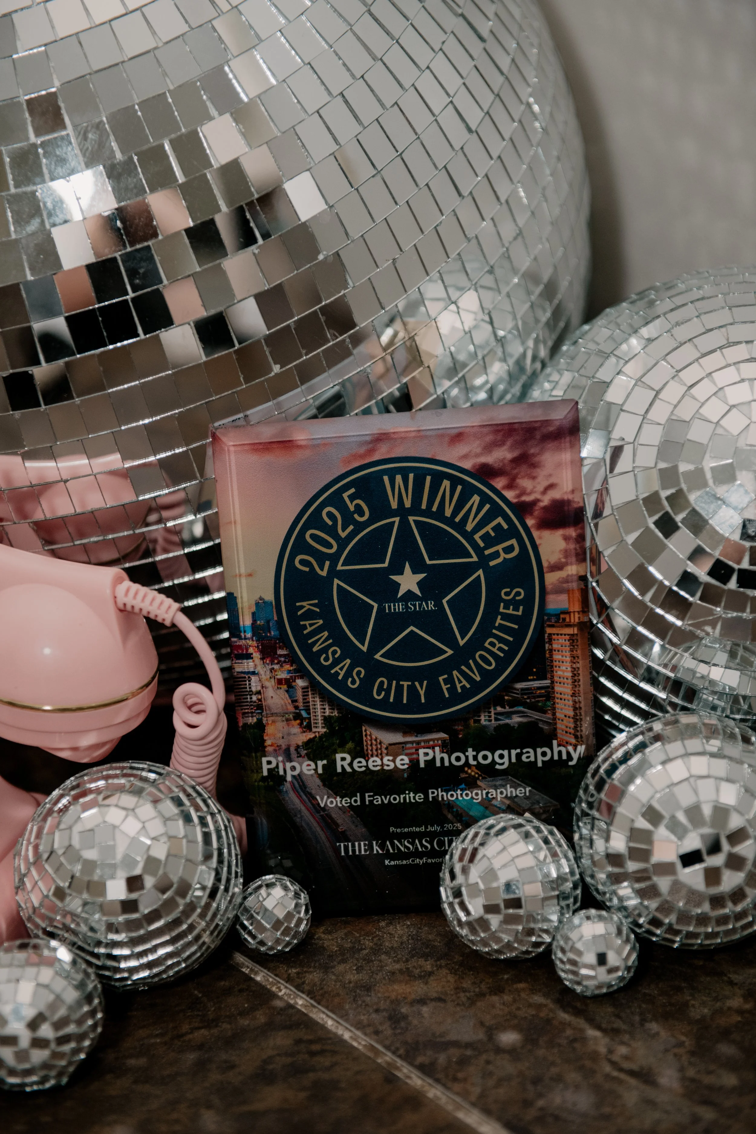 Award plaque with a star and circular text that says '2025 Winner Kansas City Favorites, Piper Reese Photography, Voted Favorite Photographer' surrounded by small and large disco balls and pink telephone.