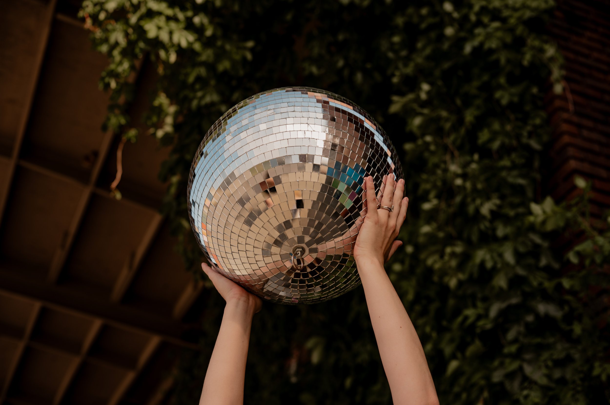 Person holding a large disco ball with green foliage background under a carport in Kansas City, Missouri