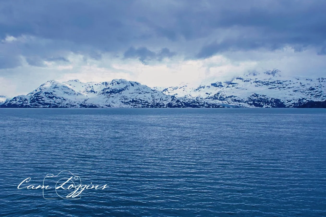 A large body of water with snow-capped mountains in the distance under a cloudy sky, with the words 'Camp Logan' written in cursive in the lower left corner.