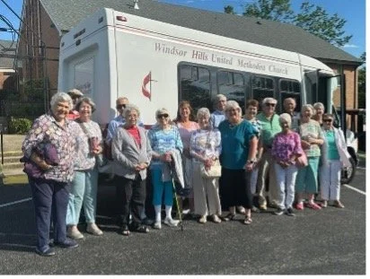 Group of elderly people standing in front of a mobile church vehicle labeled 'Windsor Hills United Methodist Church'.
