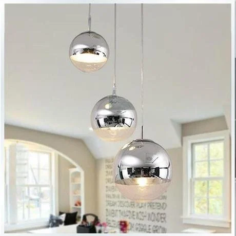 Three shiny silver spherical pendant lights hanging from the ceiling in a bright room with large windows and white walls.