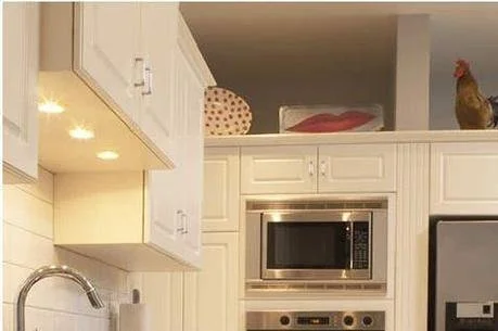 Close-up of a kitchen with white cabinets, a microwave, and a hen standing on top of the cabinets.