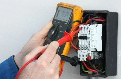 Person using a multimeter to test electrical wiring inside a black electrical box.