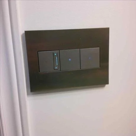 Wall-mounted control panel with three touchscreen switches inside a dark frame