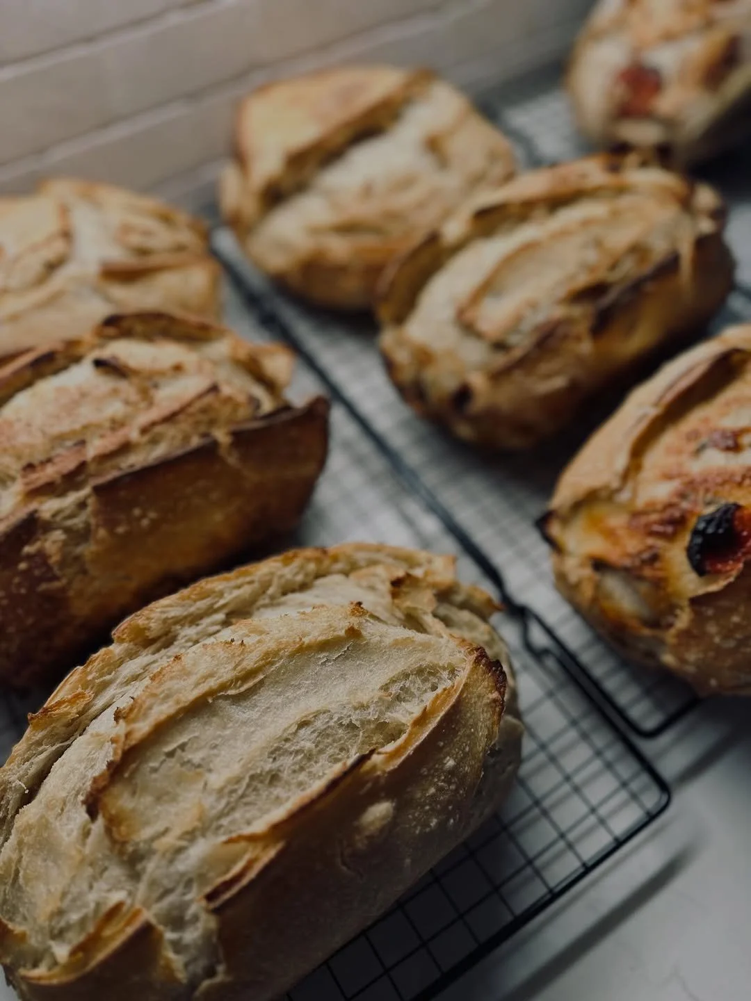 Multiple partially sliced loaves of bread cooling on wire racks.
