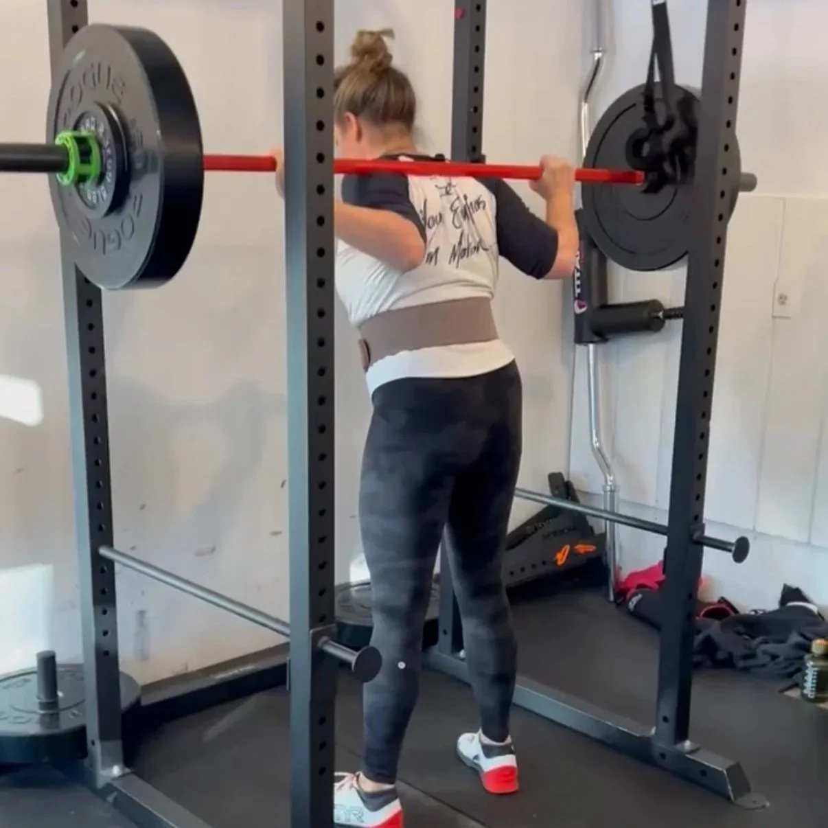 Woman lifting a barbell during a workout in a gym. She is wearing workout clothes and standing inside a power rack.