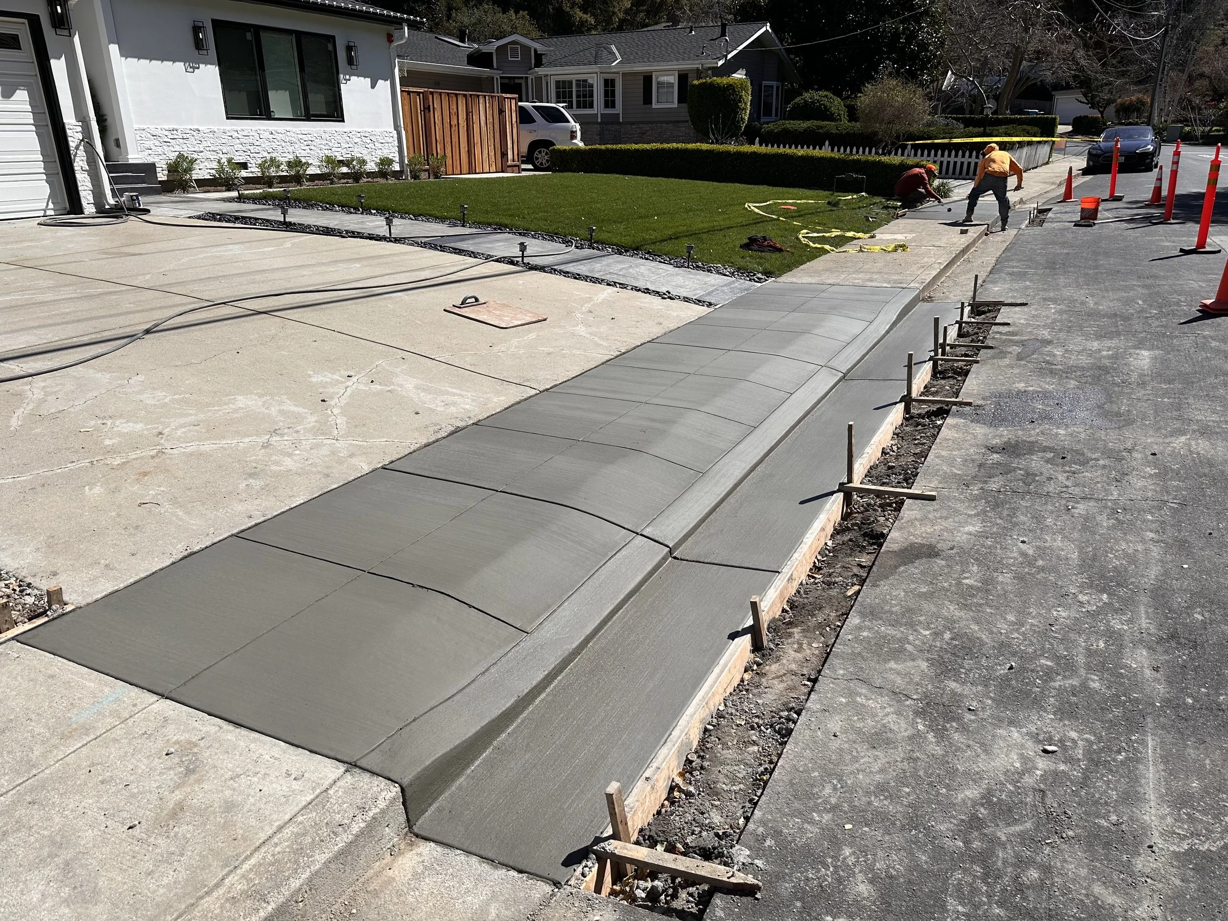 Construction workers paving a new sidewalk in a residential neighborhood on a sunny day.