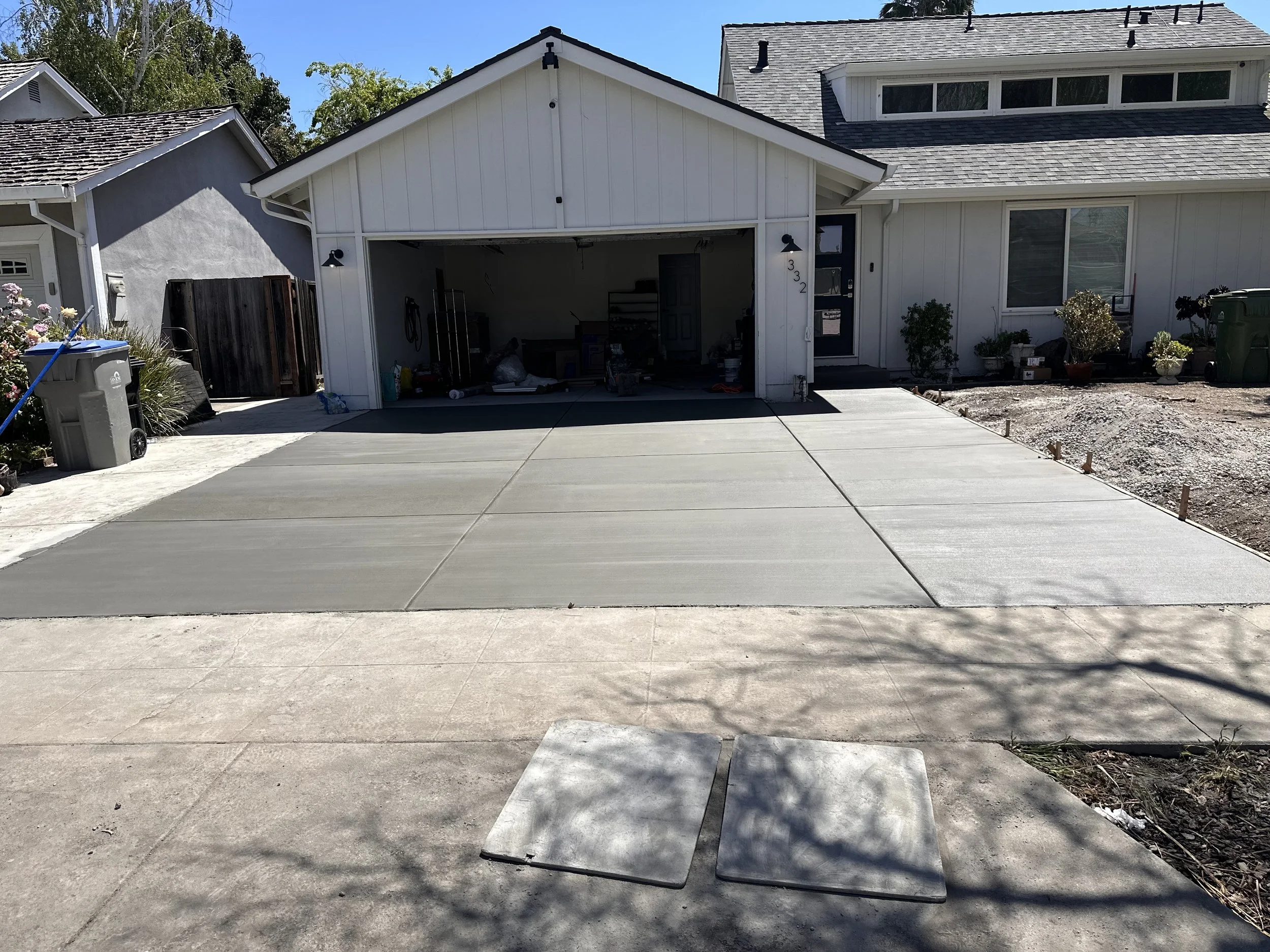 Recently poured concrete driveway and sidewalk in front of a white house with a garage