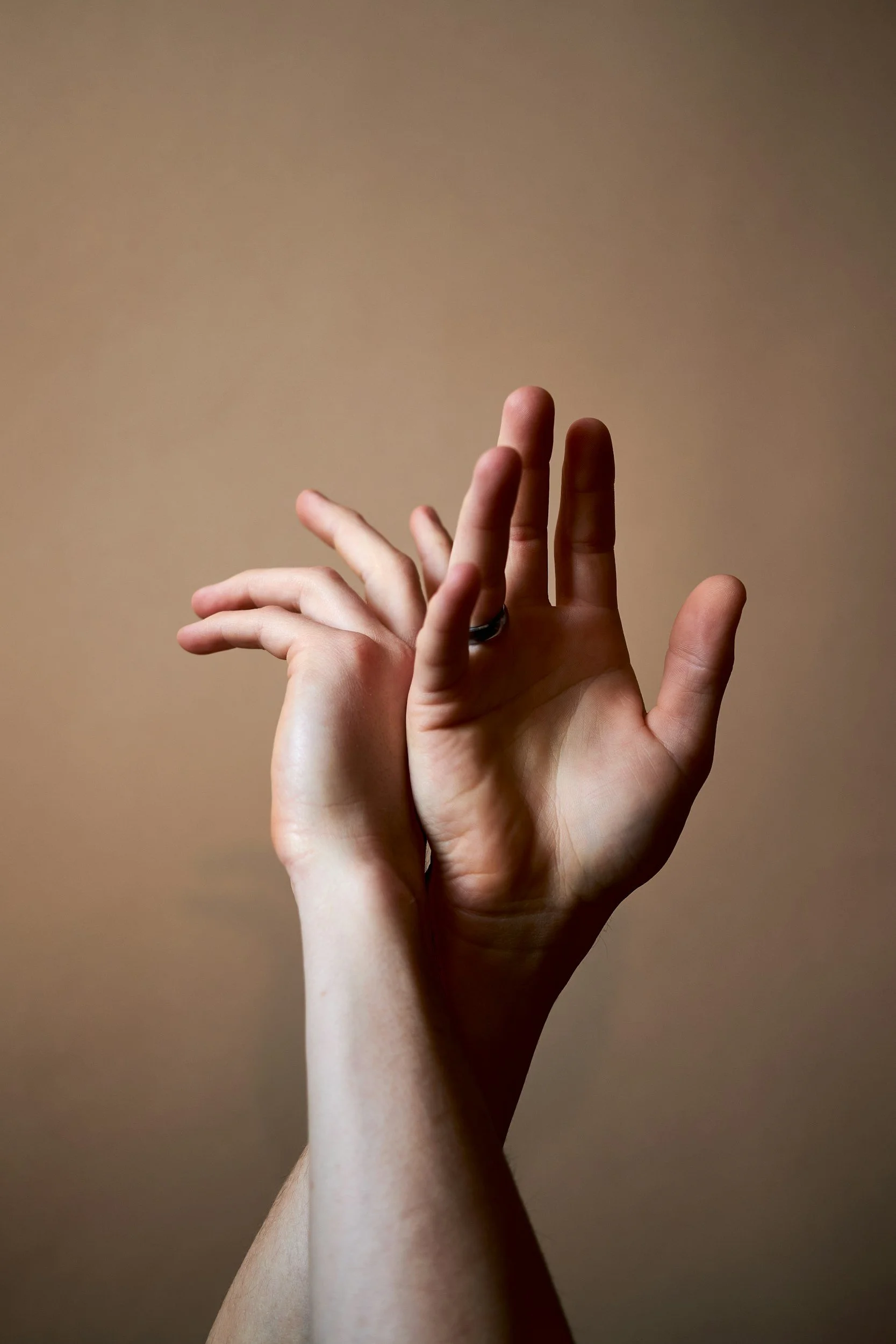 Close-up of two hands with fingers gently intertwined, placed against a plain, warm beige background.