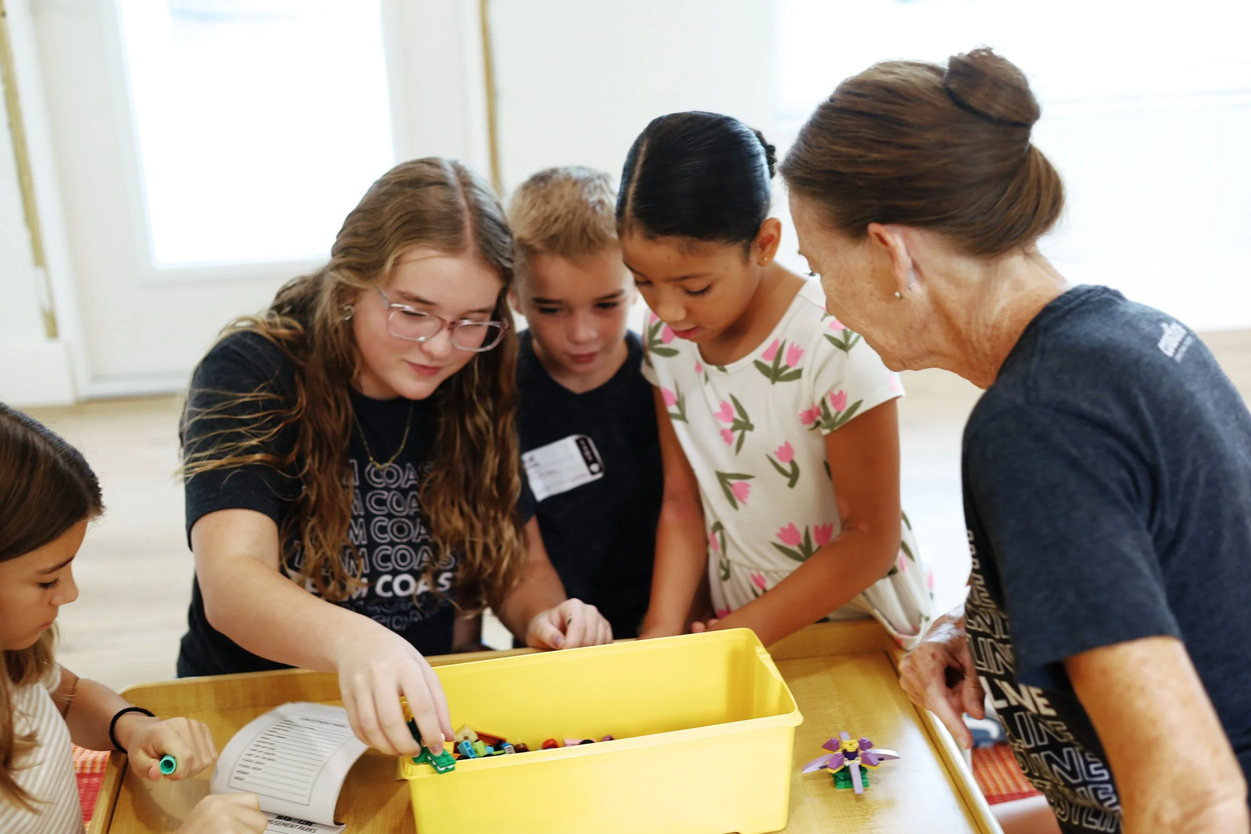 A group of kids surrounding two Coastline kids volunteers playing with legos.