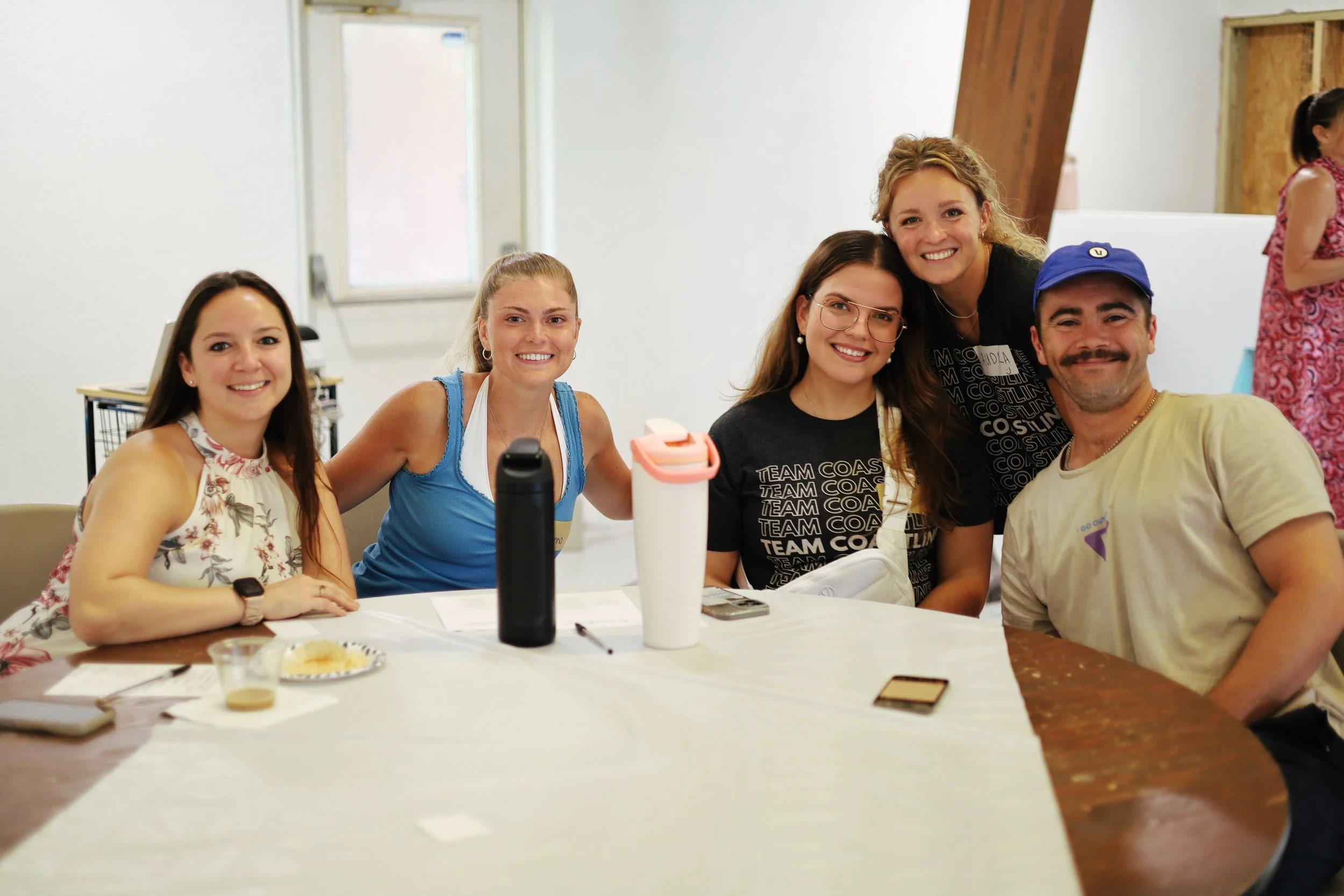 a group of young adults sitting around a table smiling as they attend discover coastline. an event to learn about church and how to get plugged in.