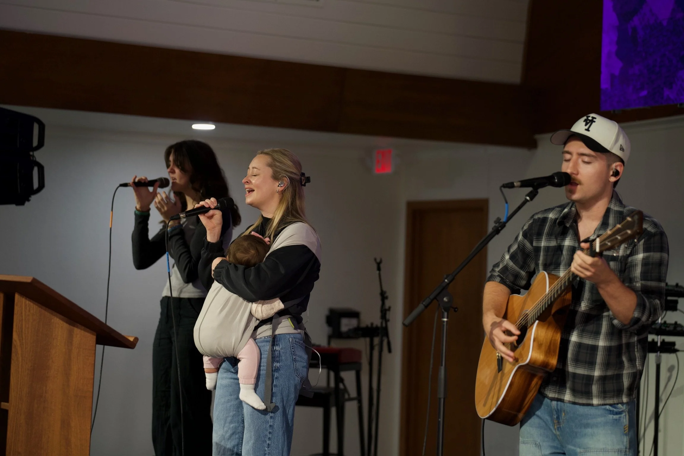 A woman singing and holding her baby while leading worship at a church in sarasota called Coastline