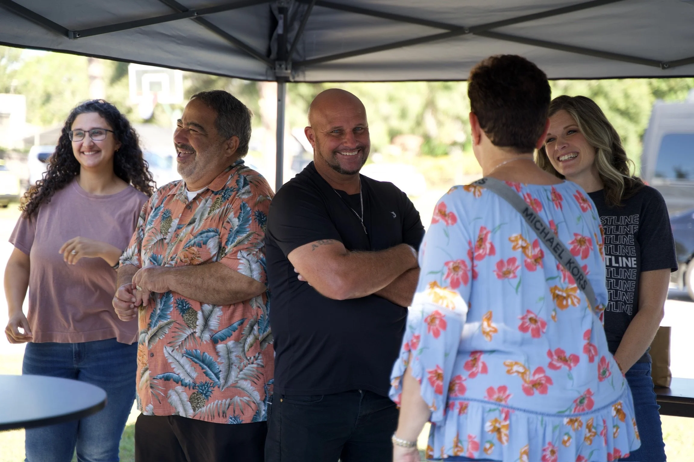 A group of six people standing and smiling under a new guest welcome tent outdoors at a church in Sarasota, FL
