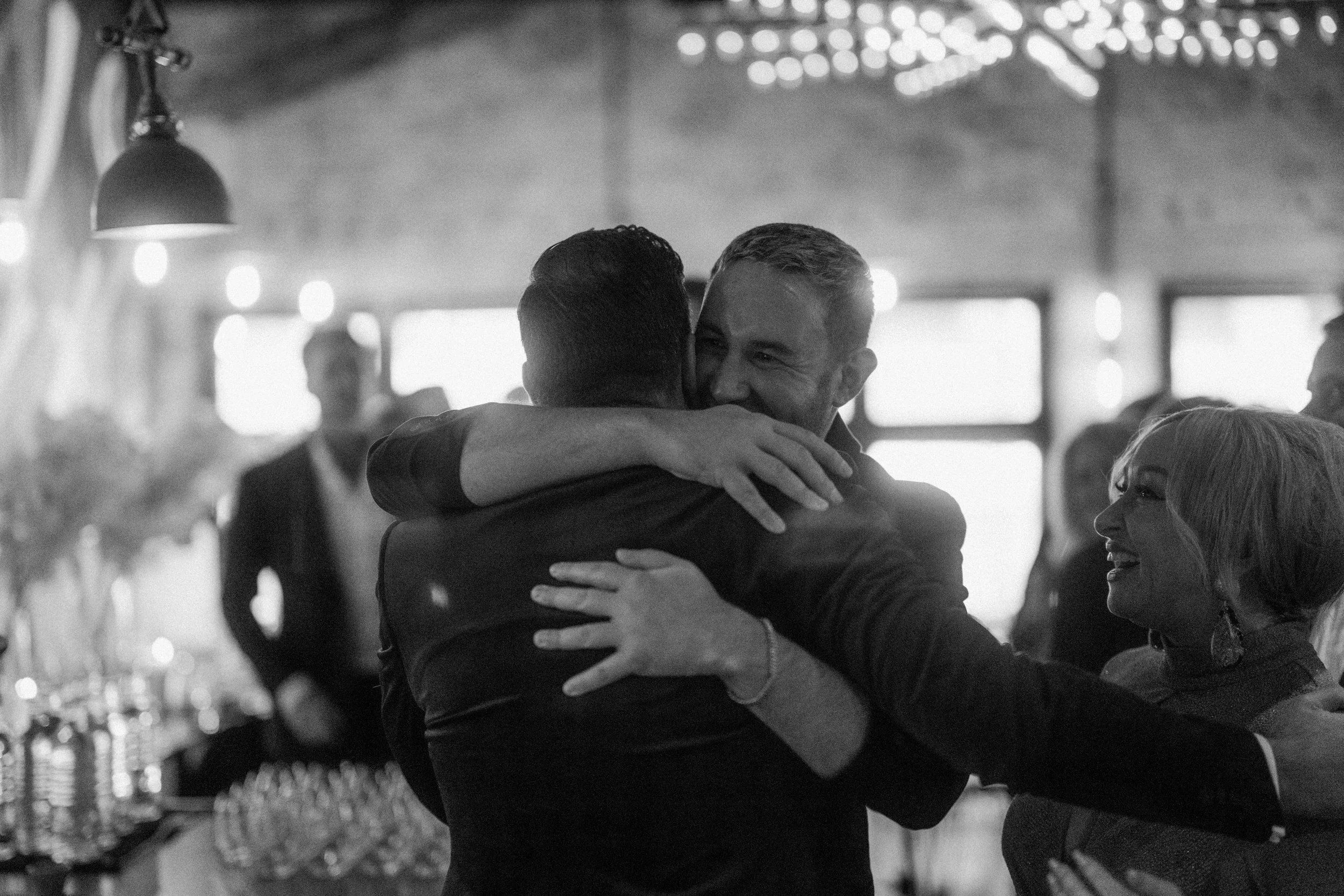 Emotional wedding photo of groom hugging friends.