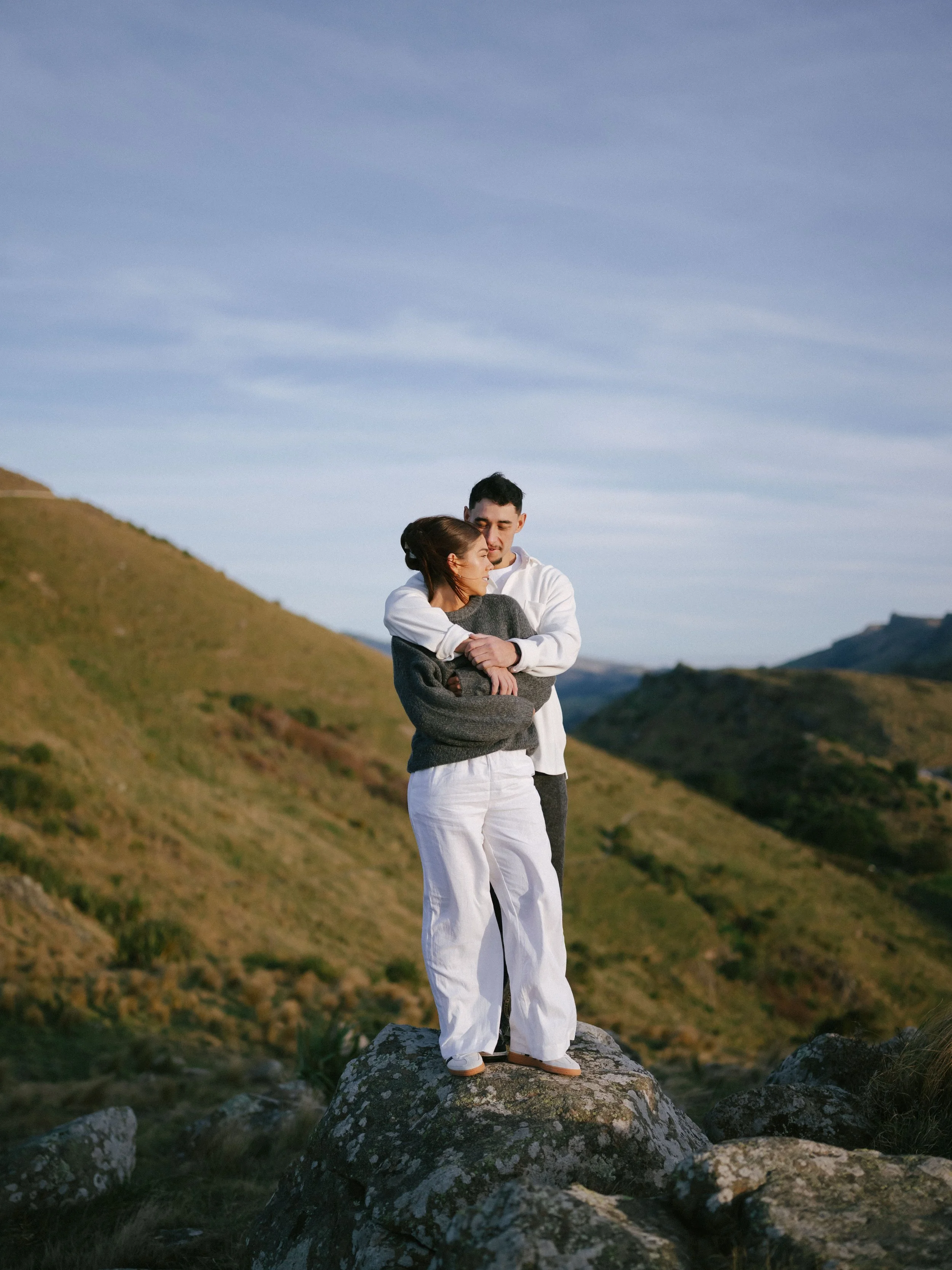 Couple wearing stylish cosy attire in a loving embrace on the Port Hills above Cashmere in Christchurch, New Zealand.