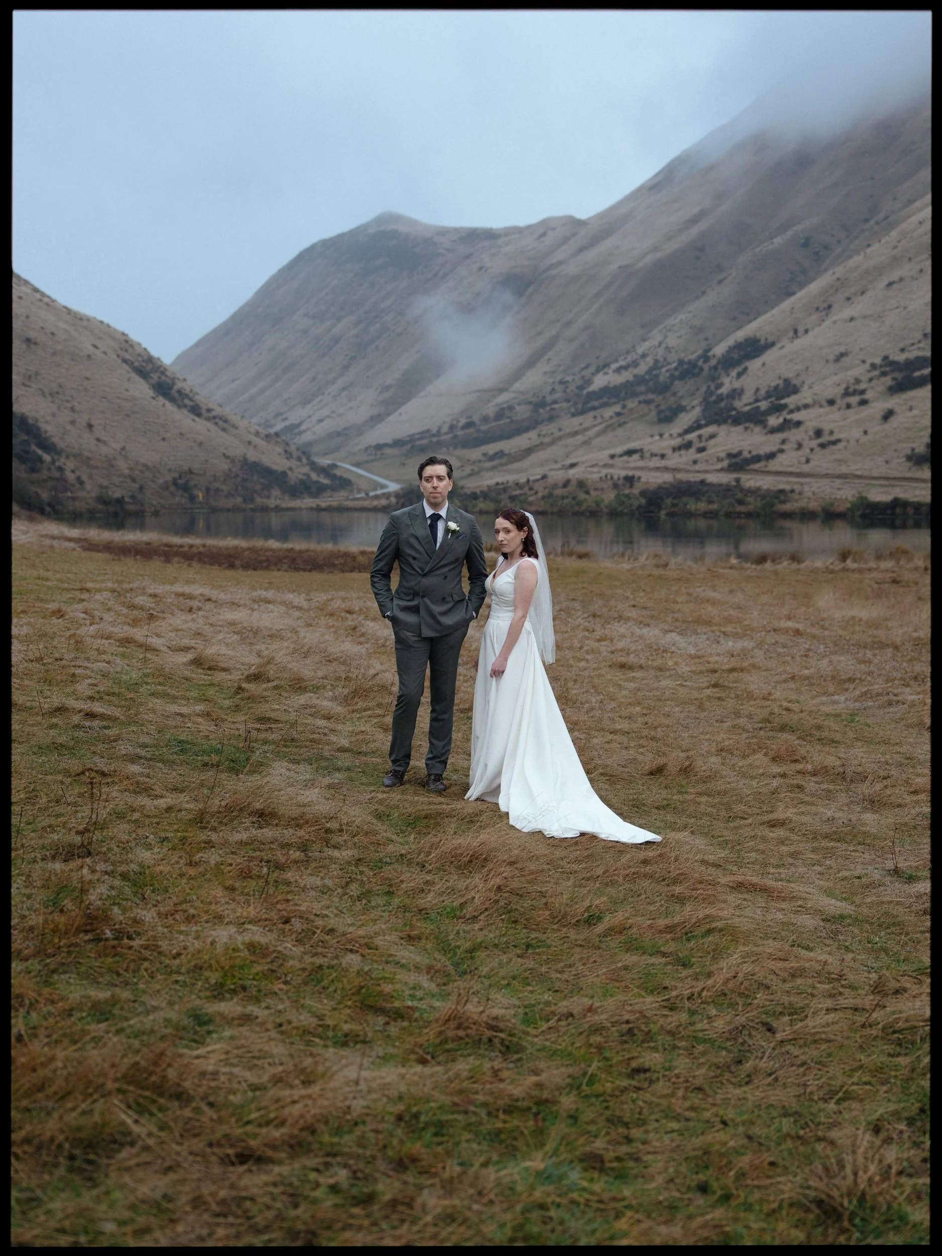 Film + Digital Wedding Photographer Queenstown - Kāmana Lakehouse, Queenstown, Otago, New Zealand. Bride and groom at Moke Lake surrounded by mountains covered in fog and cloud. Moody wedding photography.