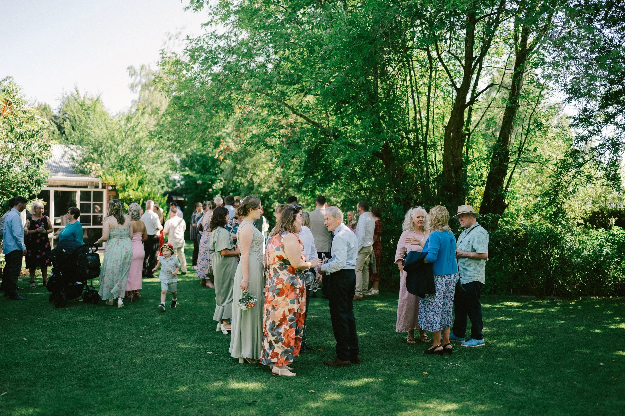 Kaiapoi Wedding, Canterbury, New Zealand.  Wedding guests talking during wedding reception on a green lawn surrounded by trees.