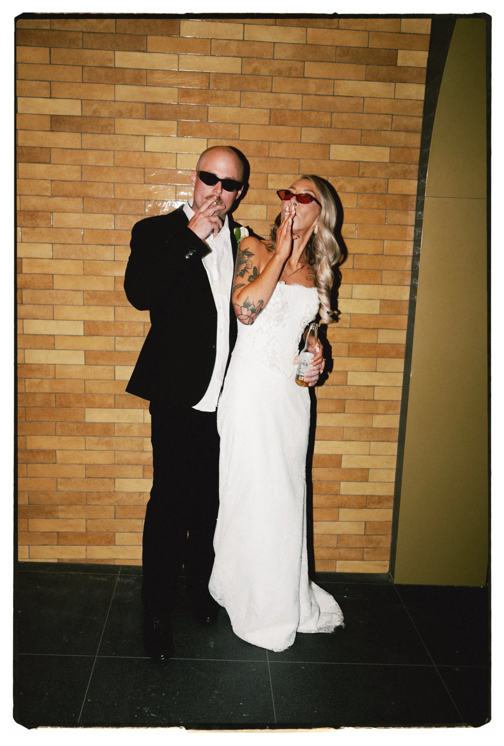 Film + Digital Wedding Photographer Christchurch - The Hilltop Wedding, Banks Peninsula, Christchurch, New Zealand. Cool flash photo of bride and groom wearing sunglasses and smoking cigarettes against yellow brick wall.