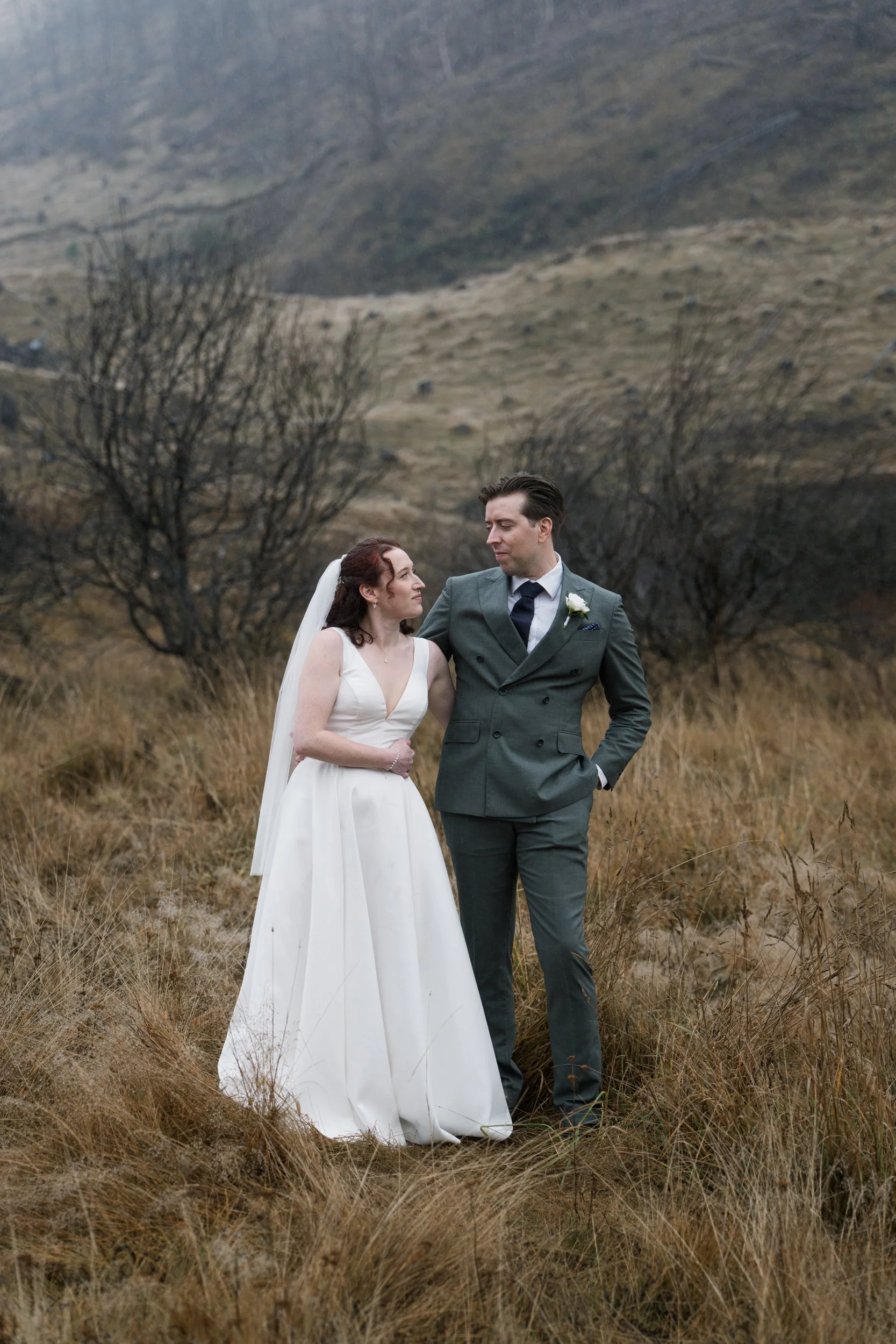 Film + Digital Wedding Photographer Queenstown - Kāmana Lakehouse, Queenstown, Otago, New Zealand. Bride and groom looking at each other at Moke Lake with dead trees and mountains in the background. Moody wedding photography.
