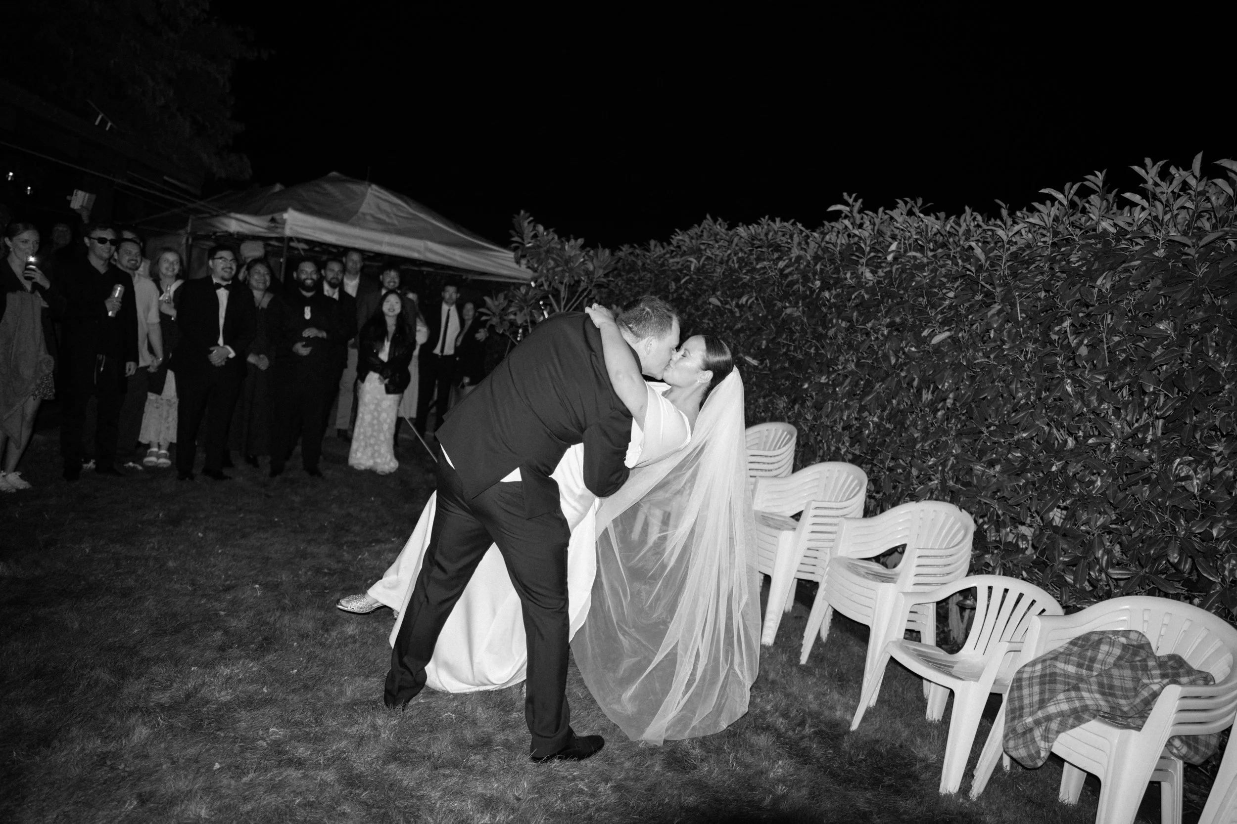 Film + Digital Wedding Photographer Christchurch - Backyard Wedding, Christchurch, Canterbury, New Zealand. Bride and groom kiss during first dance, with the groom dipping the bride. Guests in the background at backyard wedding reception.