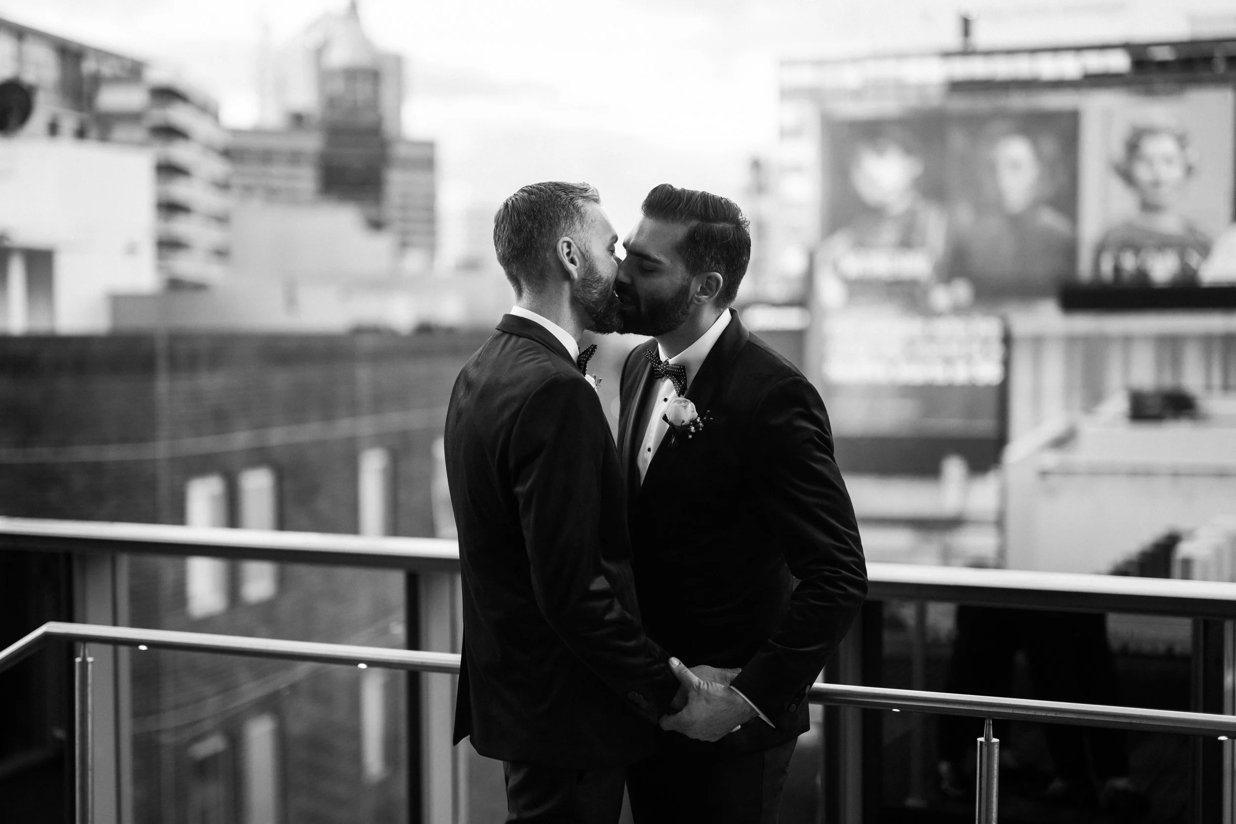 Grooms kissing on city hotel rooftop.
