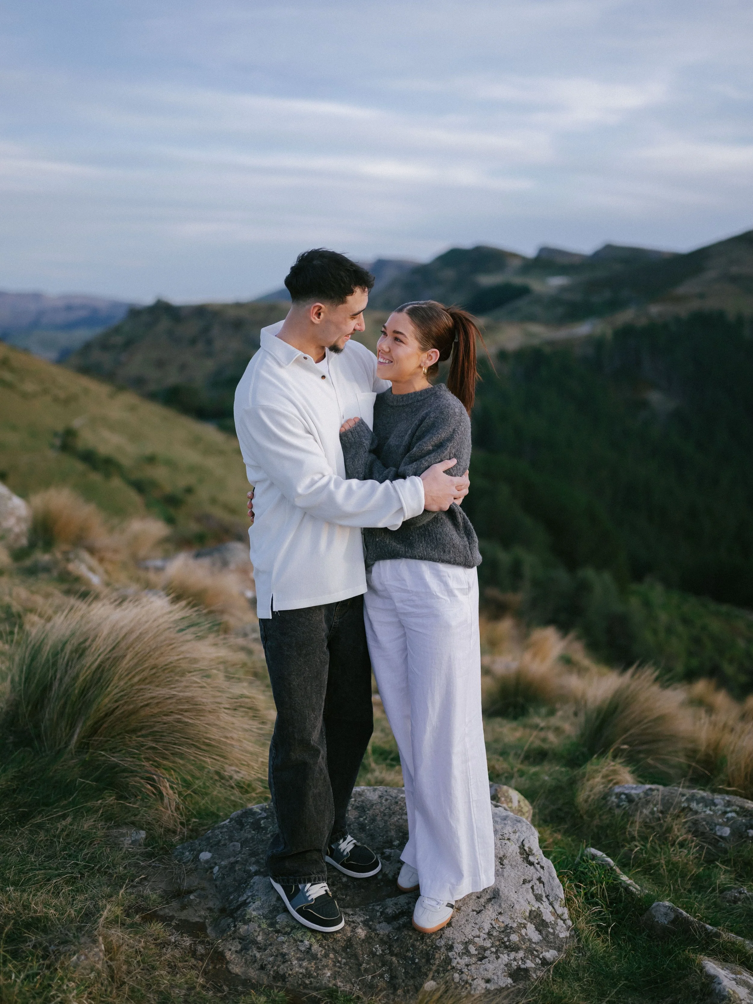 Couple wearing stylish cosy attire in a loving embrace on the Port Hills above Cashmere in Christchurch, New Zealand.