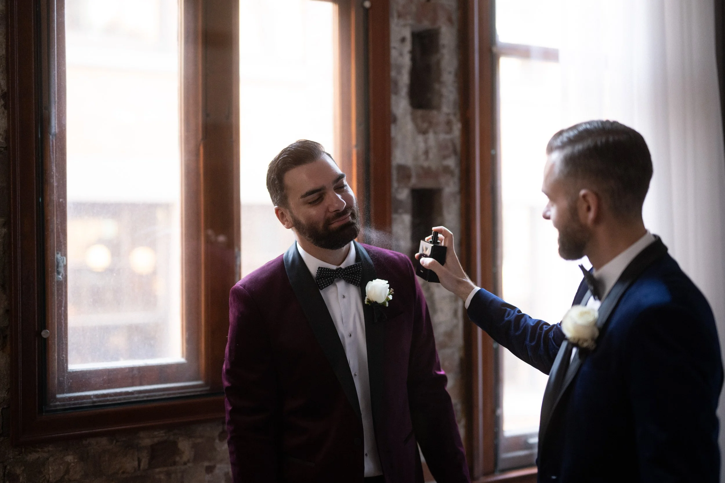 Grooms getting ready in hotel room spraying cologne.