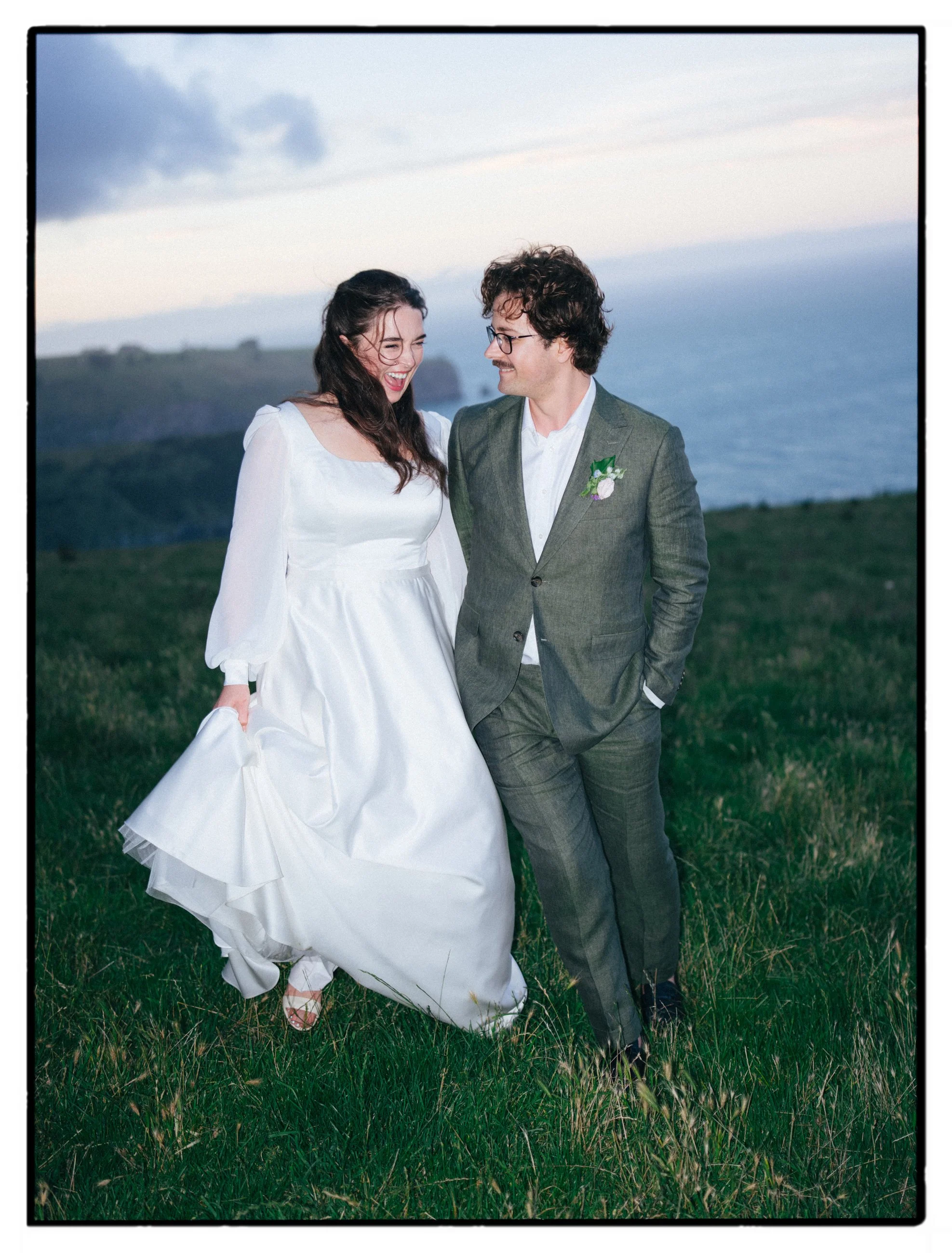 Film + Digital Wedding Photographer Christchurch - Accrington Farmhouse Wedding, Banks Peninsula, Christchurch, New Zealand. Candid film photo of bride and groom walking and smiling on a cliff with ocean in the background