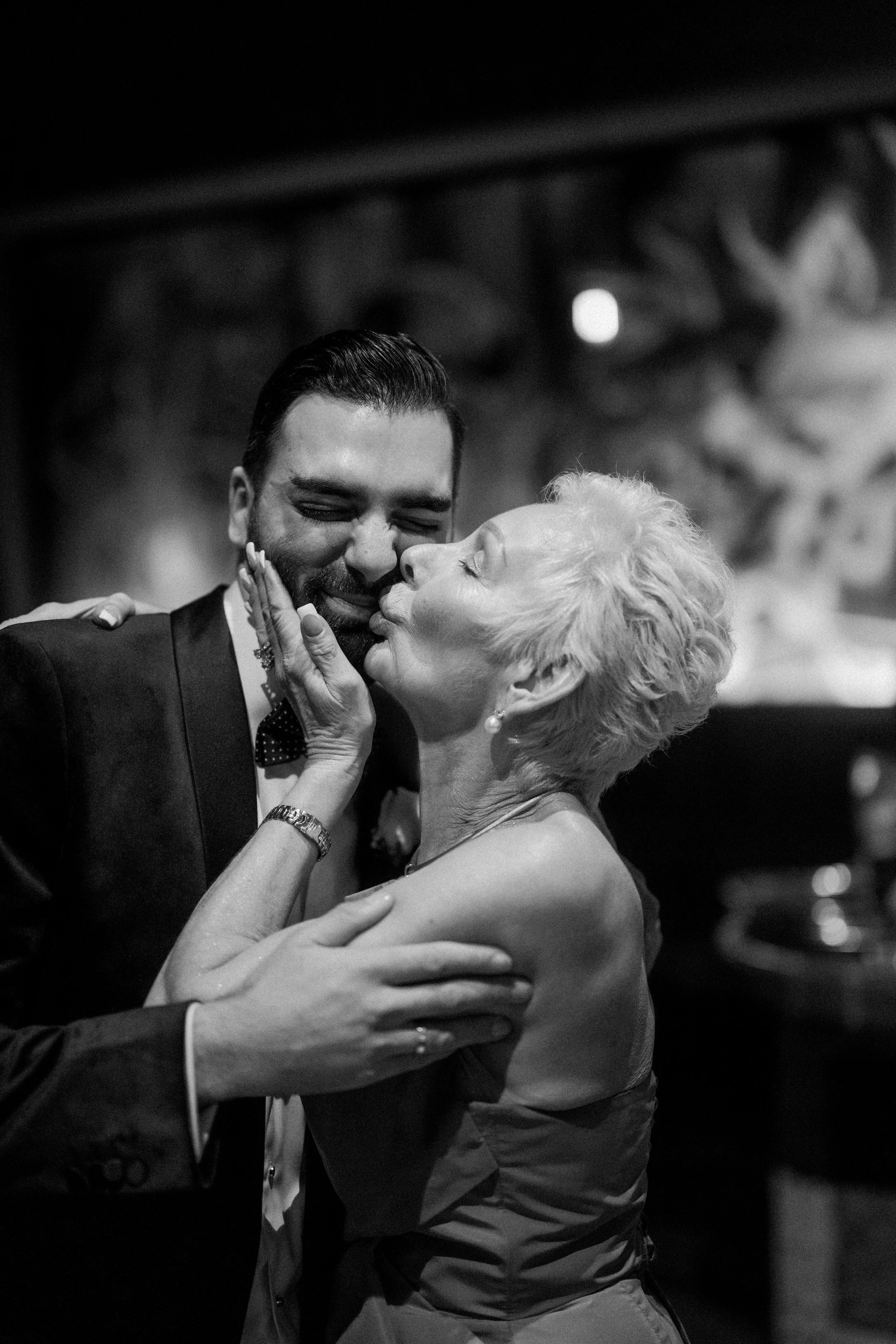 Emotional wedding photo of mum kissing groom.