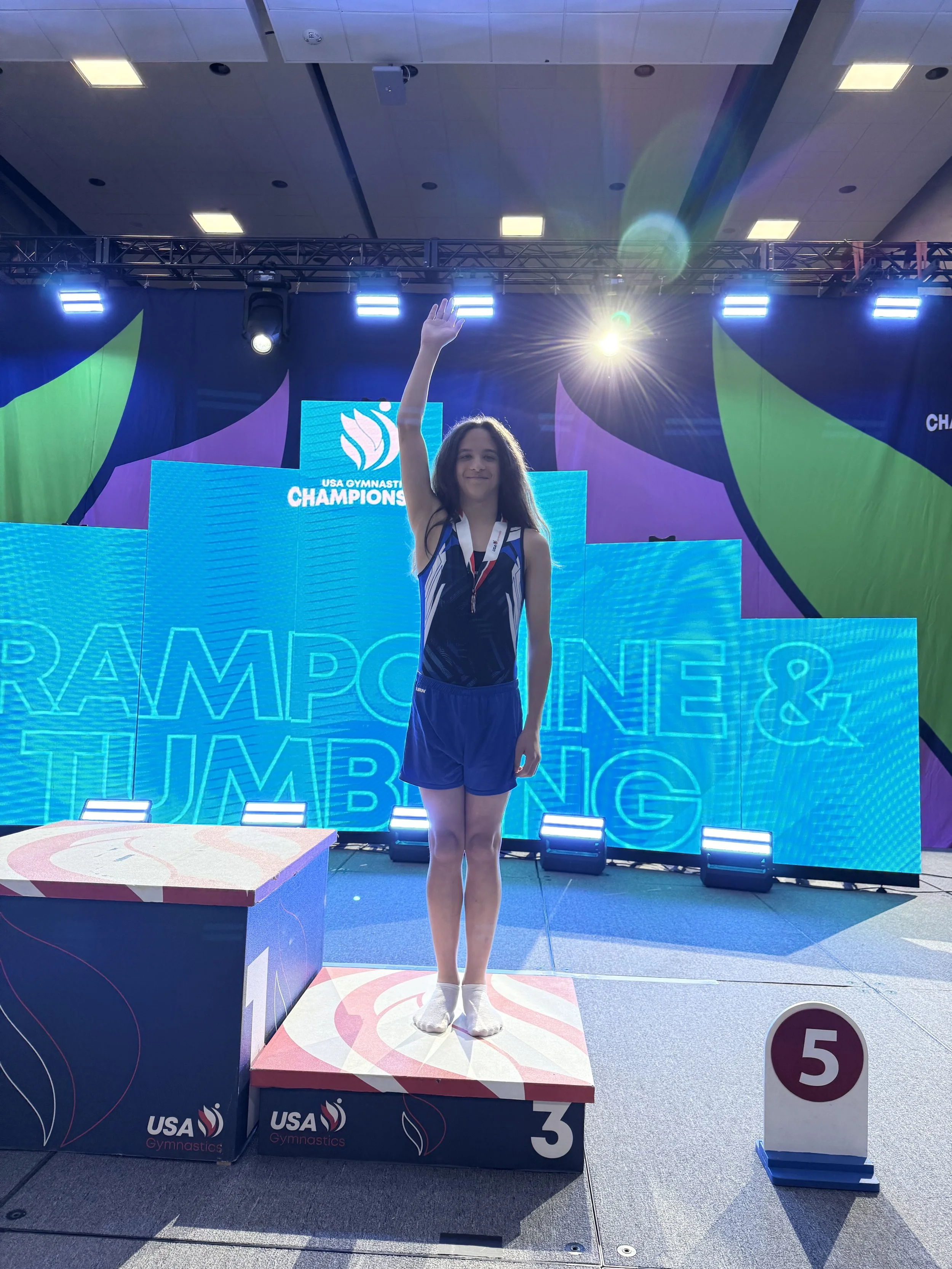 A gymnast in a blue leotard performing a handstand in front of an American flag.