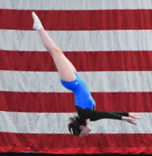 A gymnast in a blue leotard performing a handstand in front of an American flag.