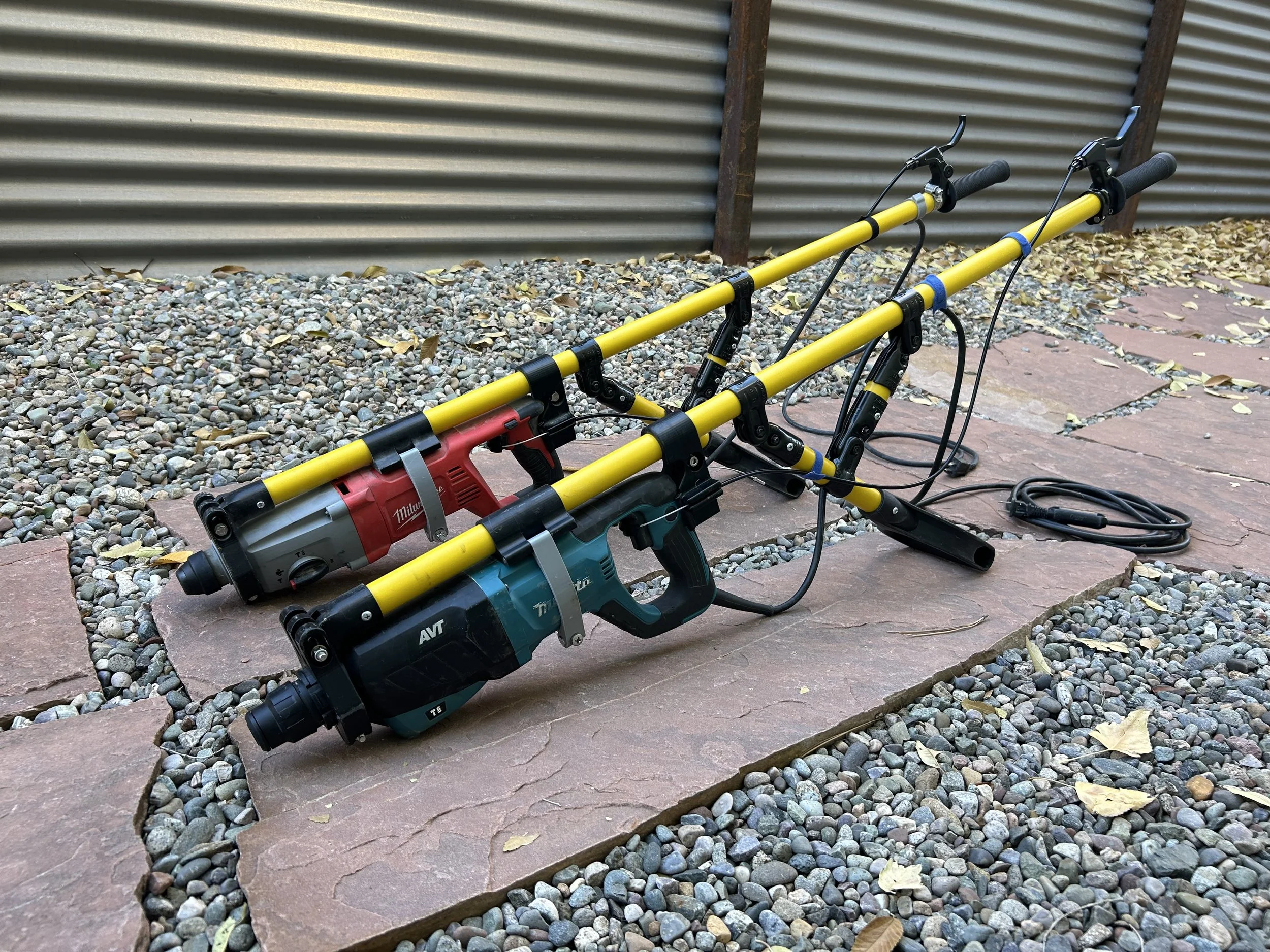 Two power tools with yellow handles and long cords resting on stone and gravel surface outside.
