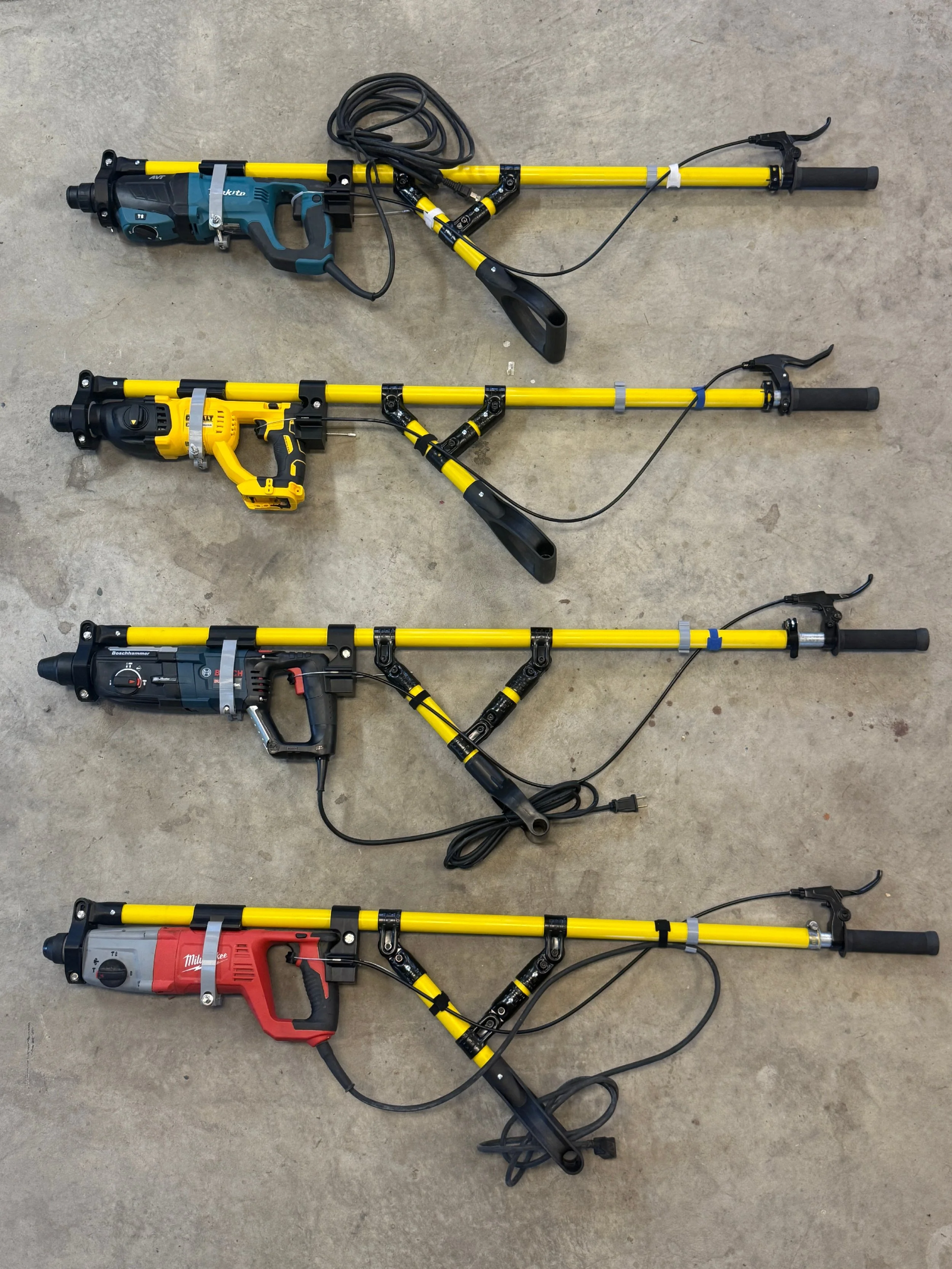 Four different rotary hammer drills with yellow shafts positioned on a concrete floor.