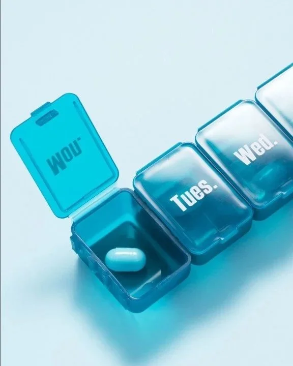 A series of four pillboxes with the days of the week and greeting words, starting with 'WOW!' for Monday, 'Tues.' for Tuesday, and 'WED.' for Wednesday. The first pillbox contains a capsule.