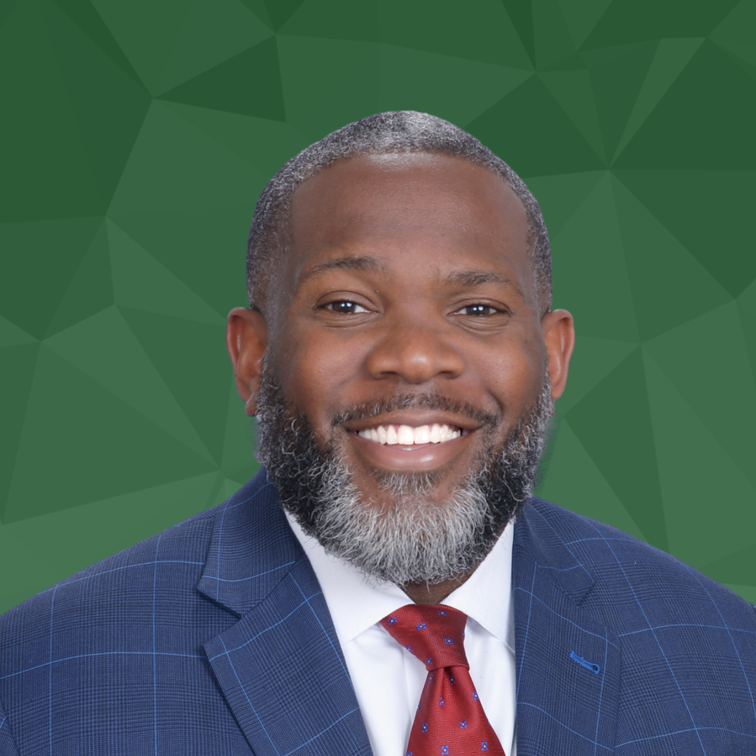 A man smiling wearing a blue suit against a green geometric background.