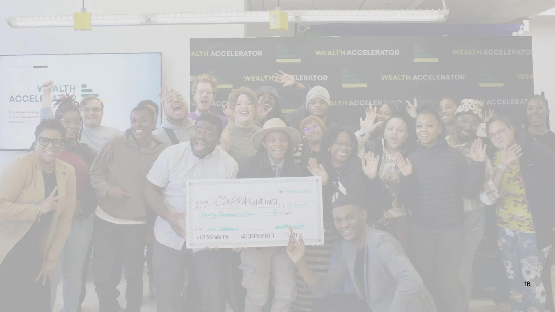 Group of people celebrating on stage with a large check, smiling and waving.