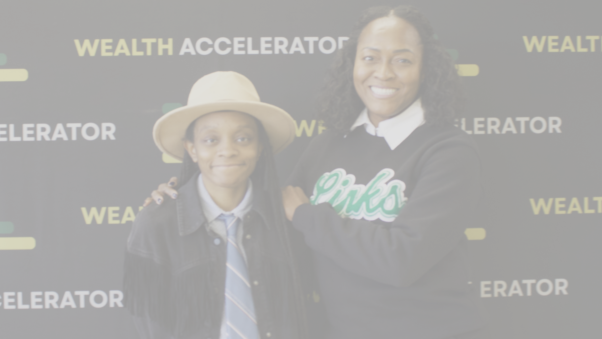A smiling woman with curly hair and a girl wearing a hat and tie, both standing in front of a black backdrop with yellow and white text that reads 'Wealth Accelerator'.