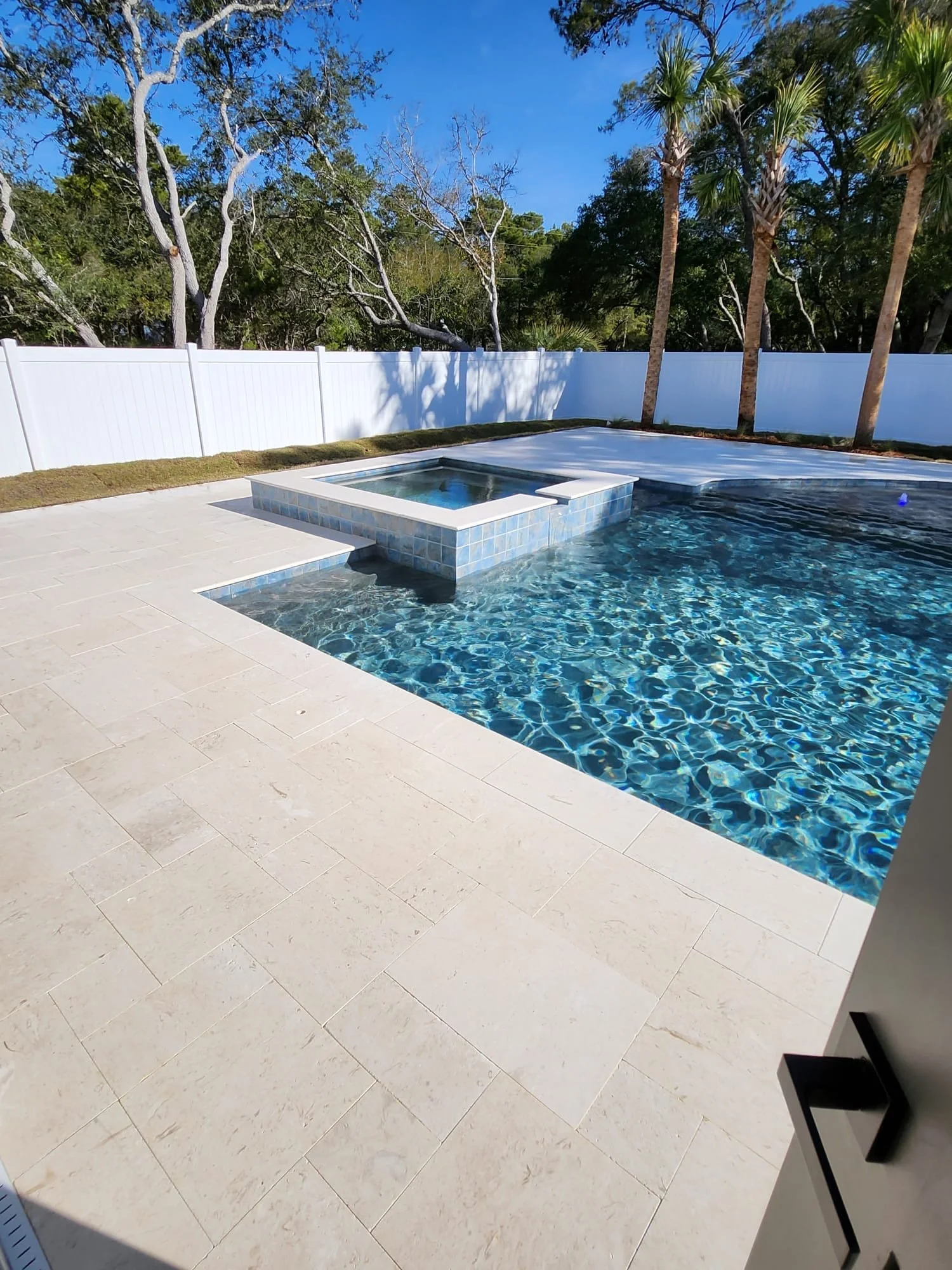 Backyard pool with a covered hot tub, white fence, and palm trees under a clear blue sky.