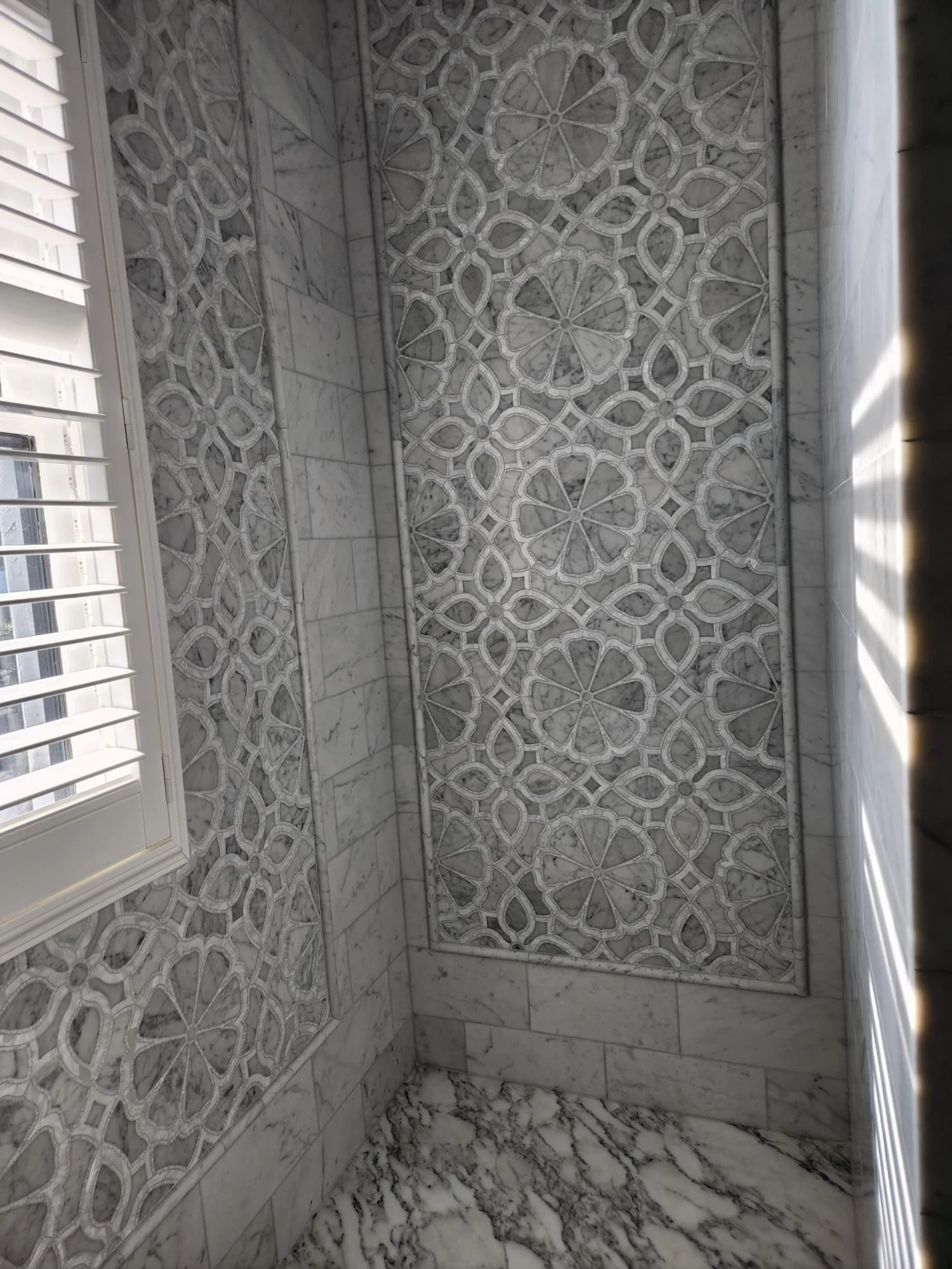 Marble bathroom with intricate geometric pattern on the walls, marble floor, and a white window shutter.
