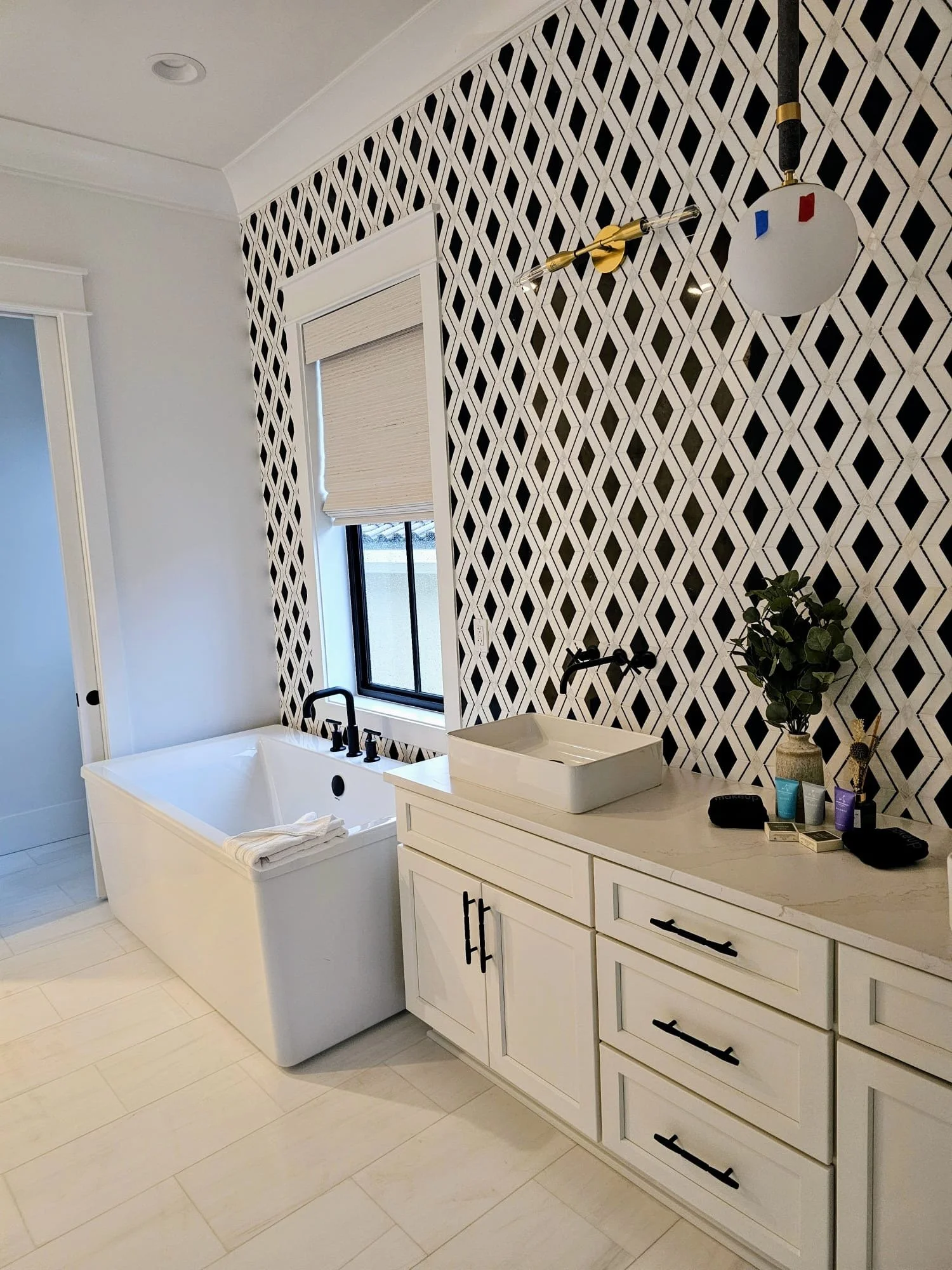 Modern bathroom with a white bathtub, a geometric black and white wallpapered wall, a vanity with a vessel sink, all done by MZ Flooring