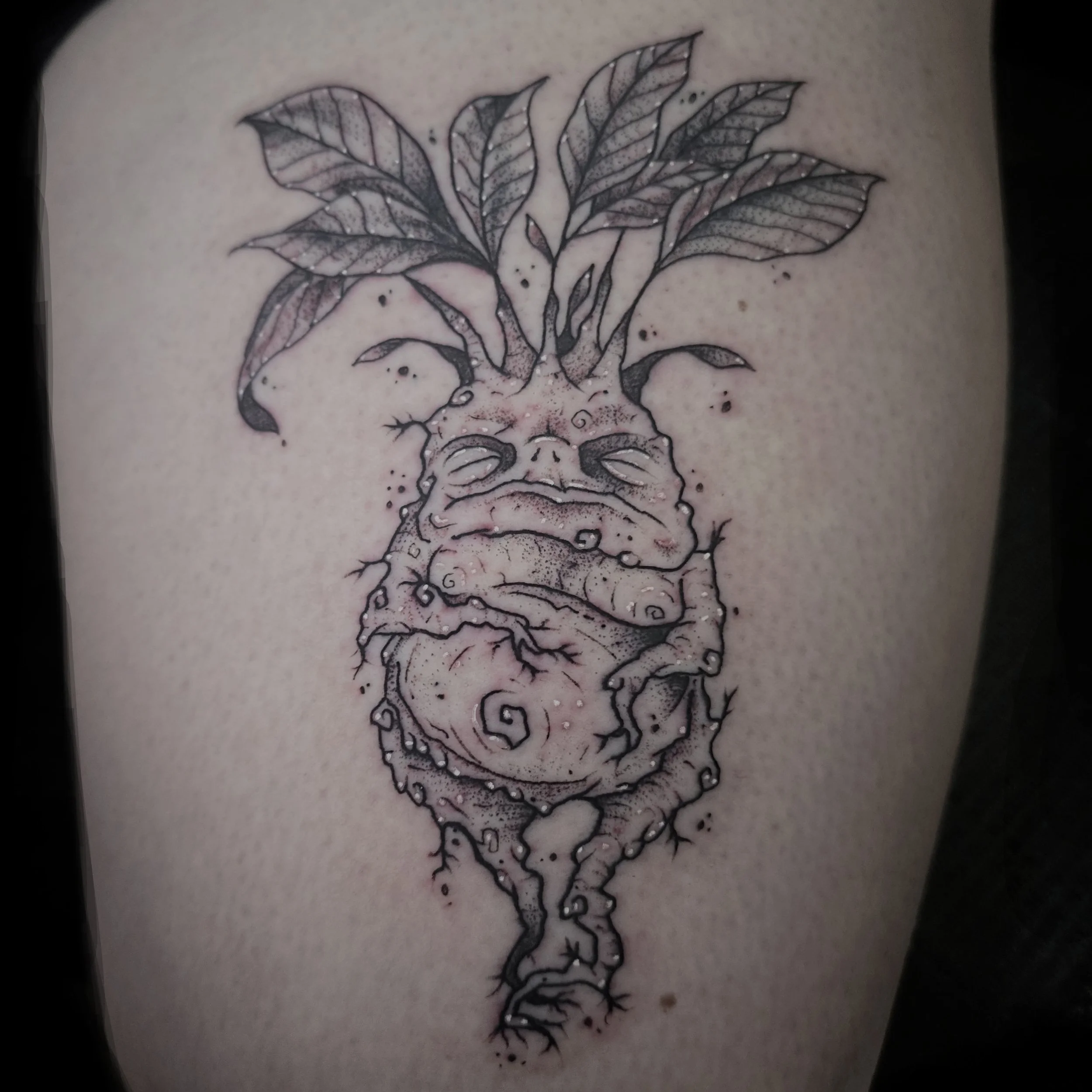 Tattoo of a root vegetable with a humanoid face and leafy top, depicted in a black and gray line art style.