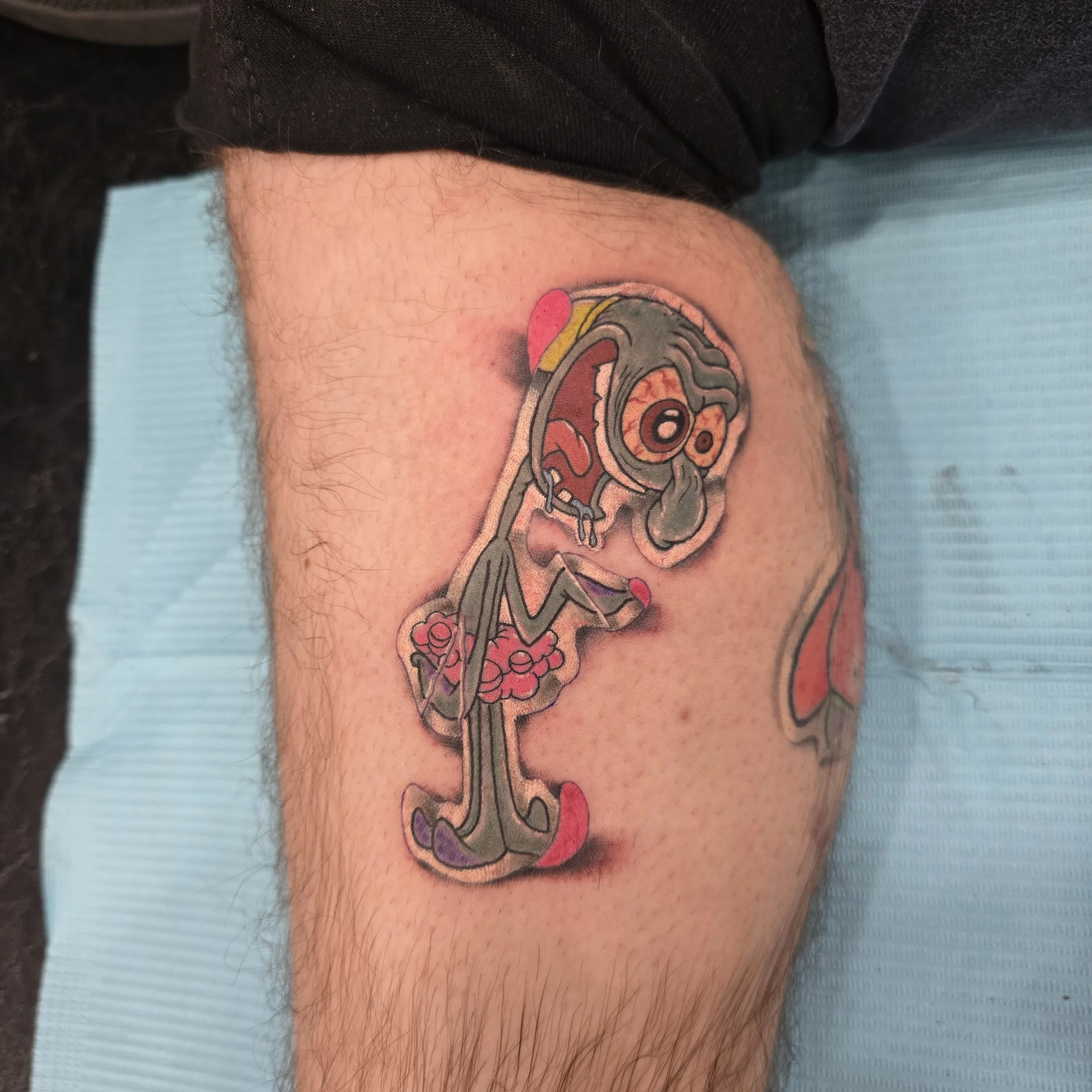 Colorful cartoon-style tattoo of a distressed, crying character with exaggerated features on person's thigh.