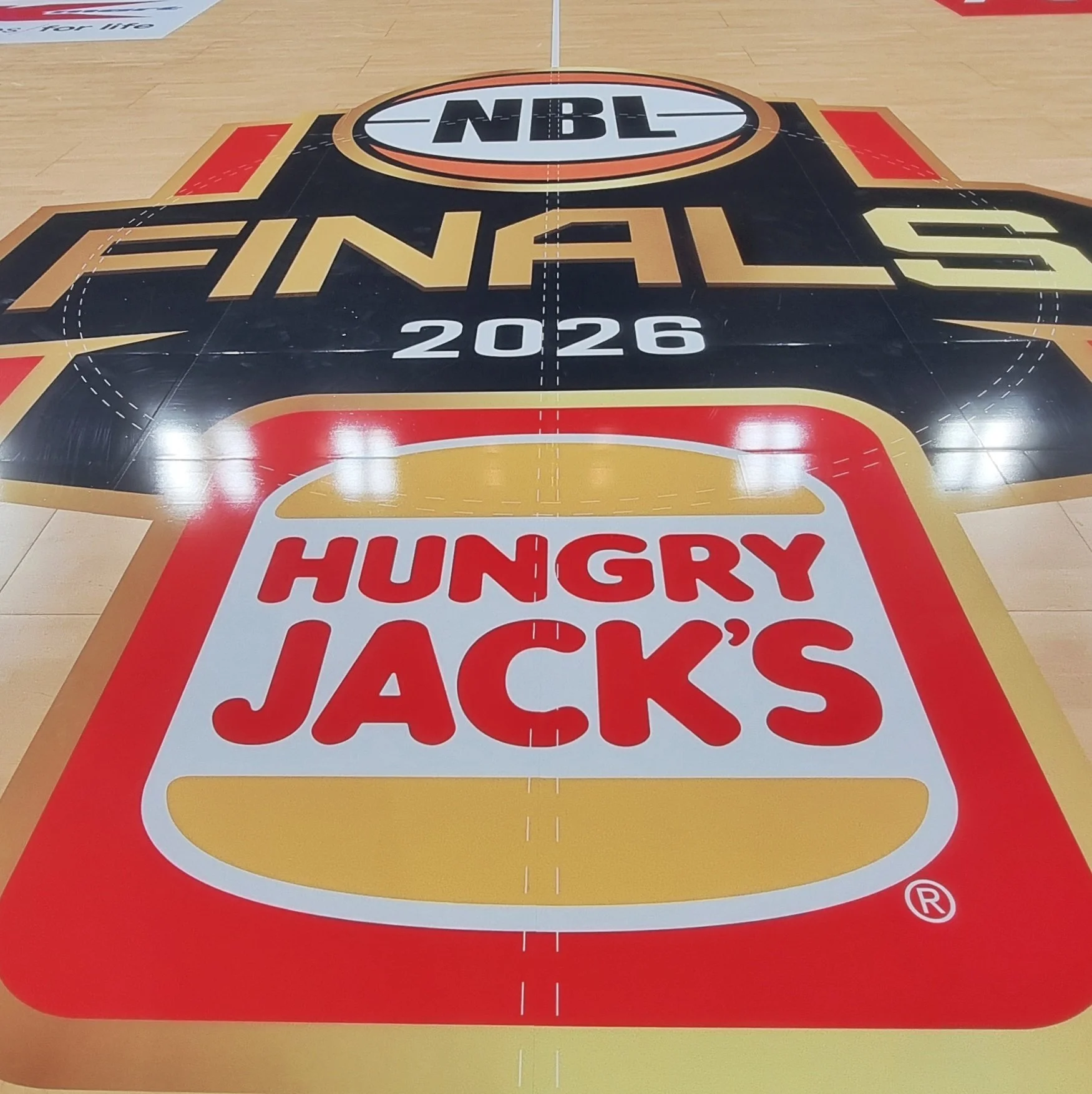 Basketball court floor with logo and text for the 2024 NBA Playoffs, sponsored by Hungry Jack's, located in an arena with advertising boards along the sidelines.