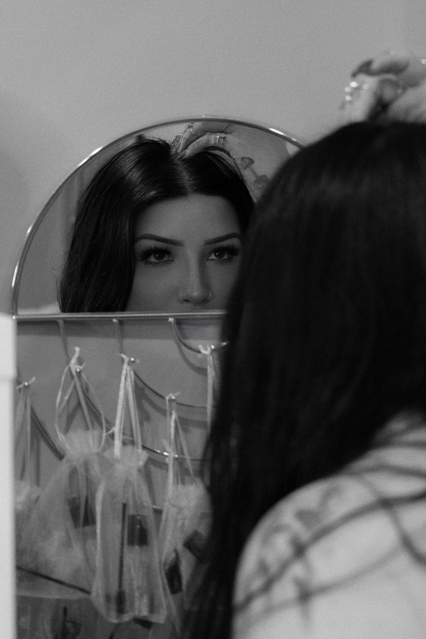 A woman with dark hair looking at herself in a mirror, with makeup brushes and cosmetics on a display in front of the mirror.