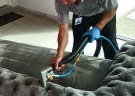 Persona usando equipo de protección y herramientas para limpiar un sofá con una aspiradora de agua.