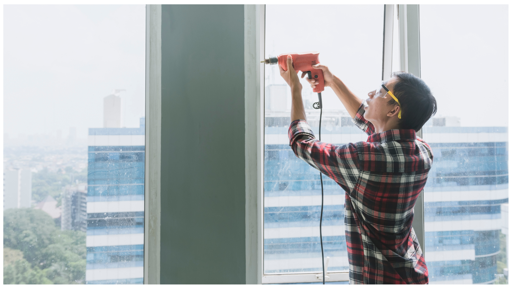 Persona usando taladro en una ventana en un edificio alto con vista a la ciudad