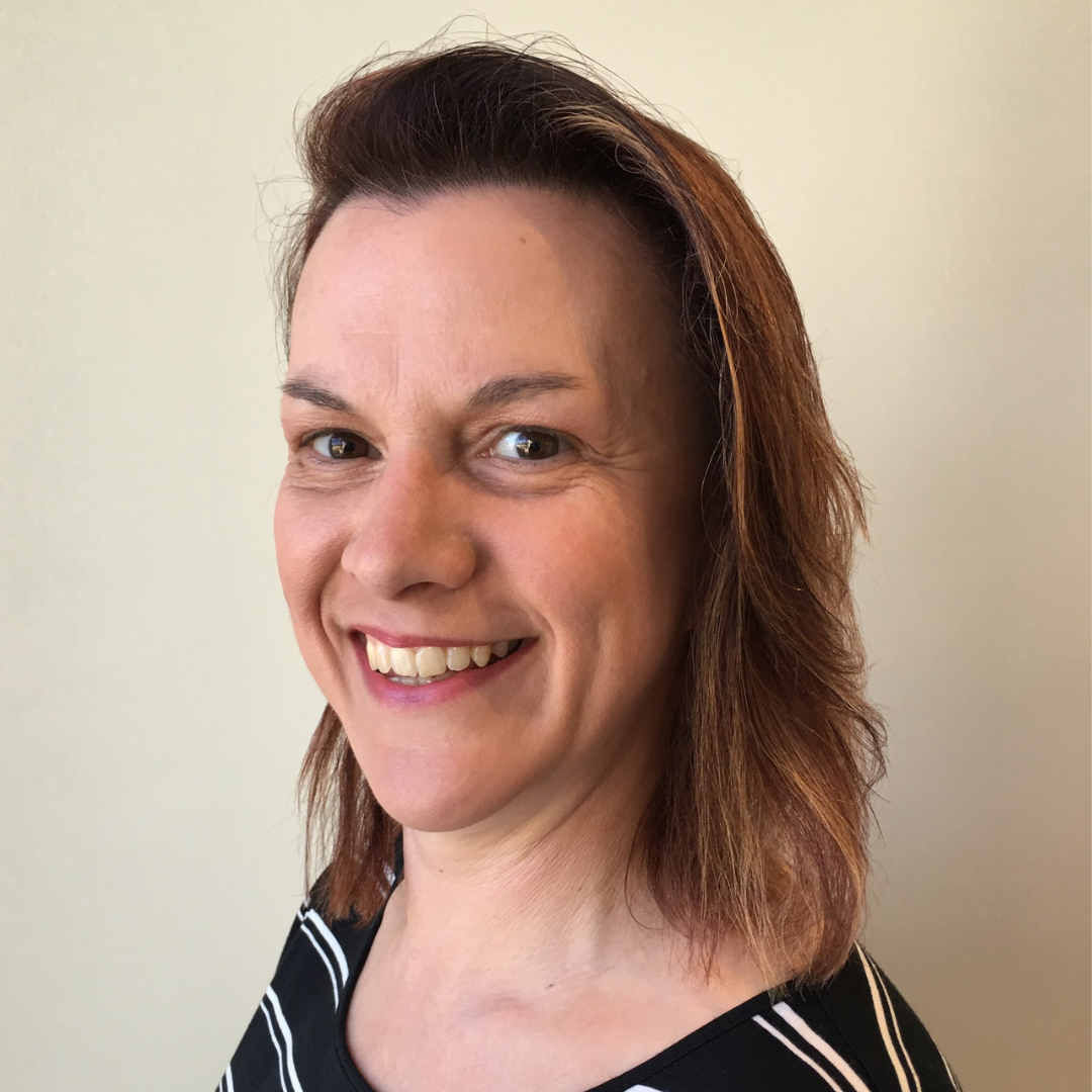 Portrait of a smiling woman with short brown hair and wearing a black and white striped top, standing against a plain light-colored wall.