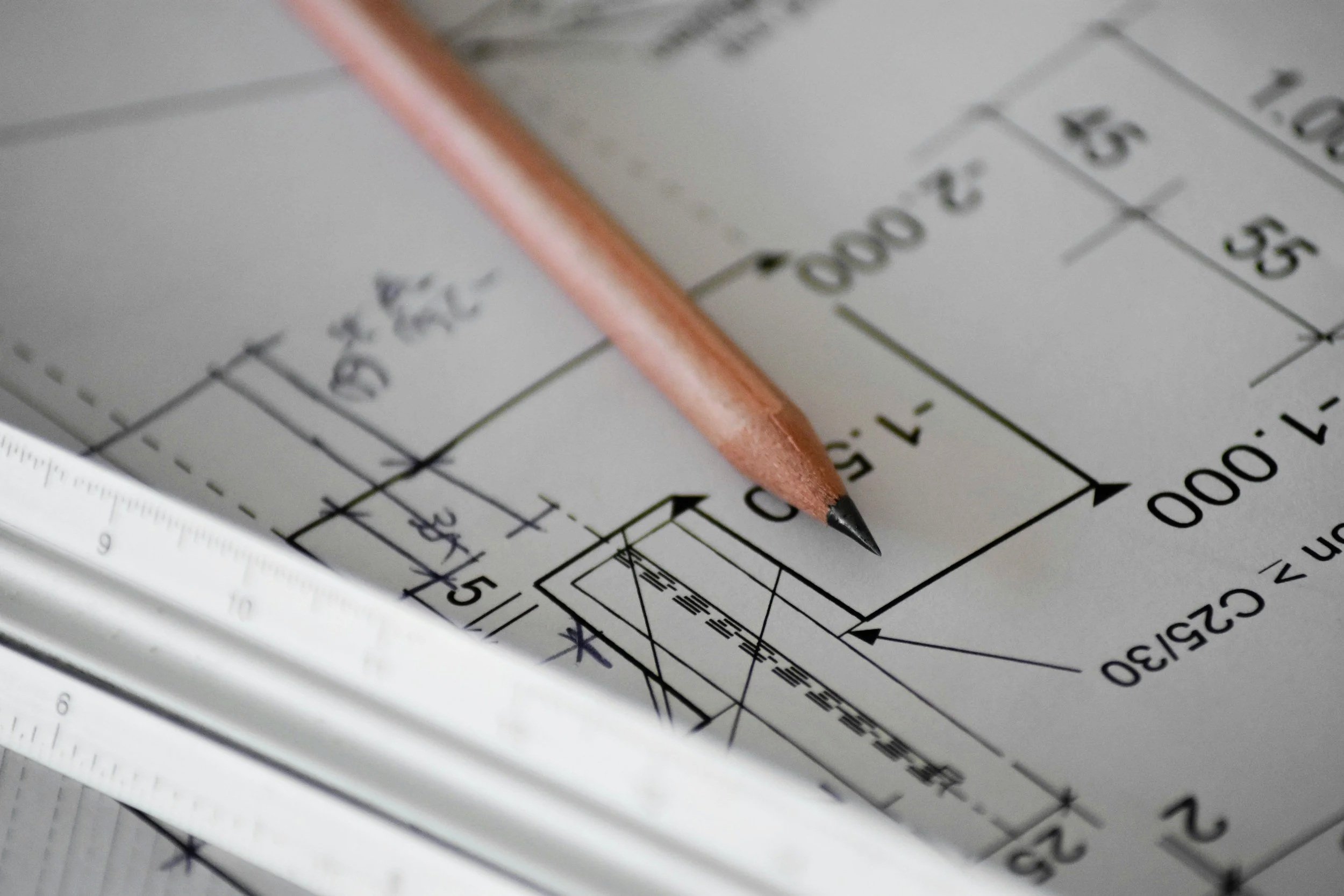 Close-up of a technical drawing or blueprint on paper, with a wooden pencil resting on top.